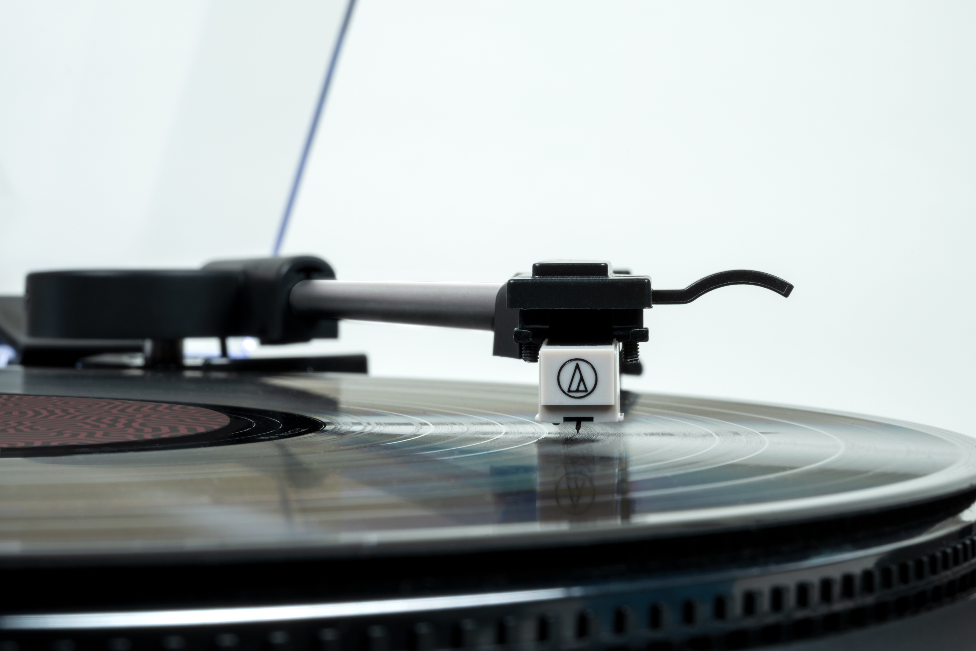 Primer plano de la aguja y el brazo de un tocadiscos en un disco de vinilo girando. El fondo es blanco.