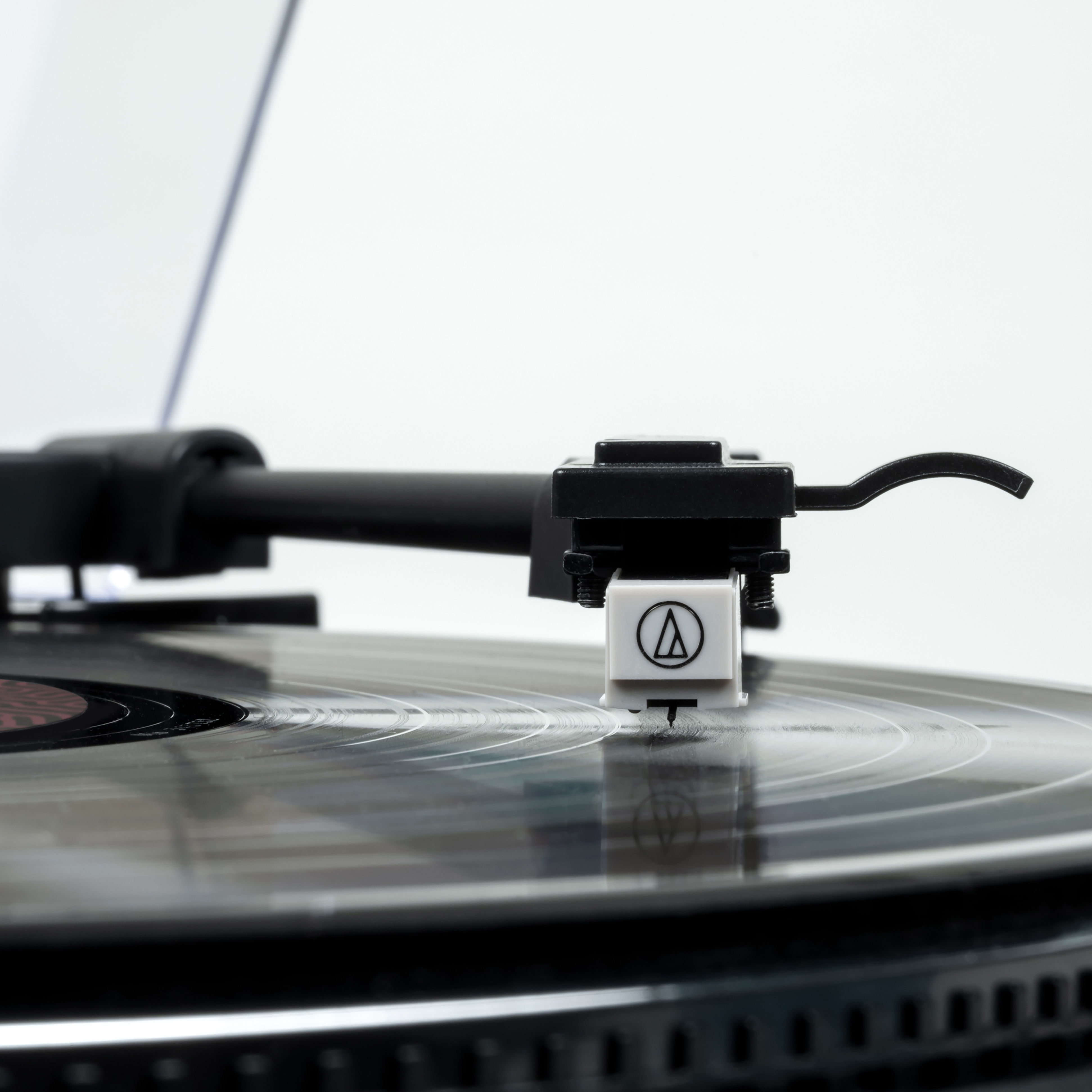 Zbliżenie igły gramofonu na płycie winylowej, widoczne logo AT, białe tło.