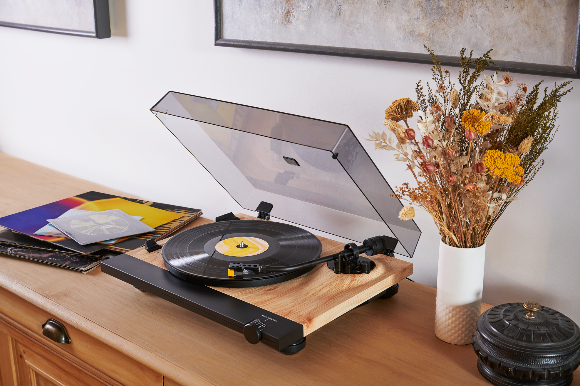 Tocadiscos con discos en superficie de madera. Un jarrón con flores secas a la derecha.