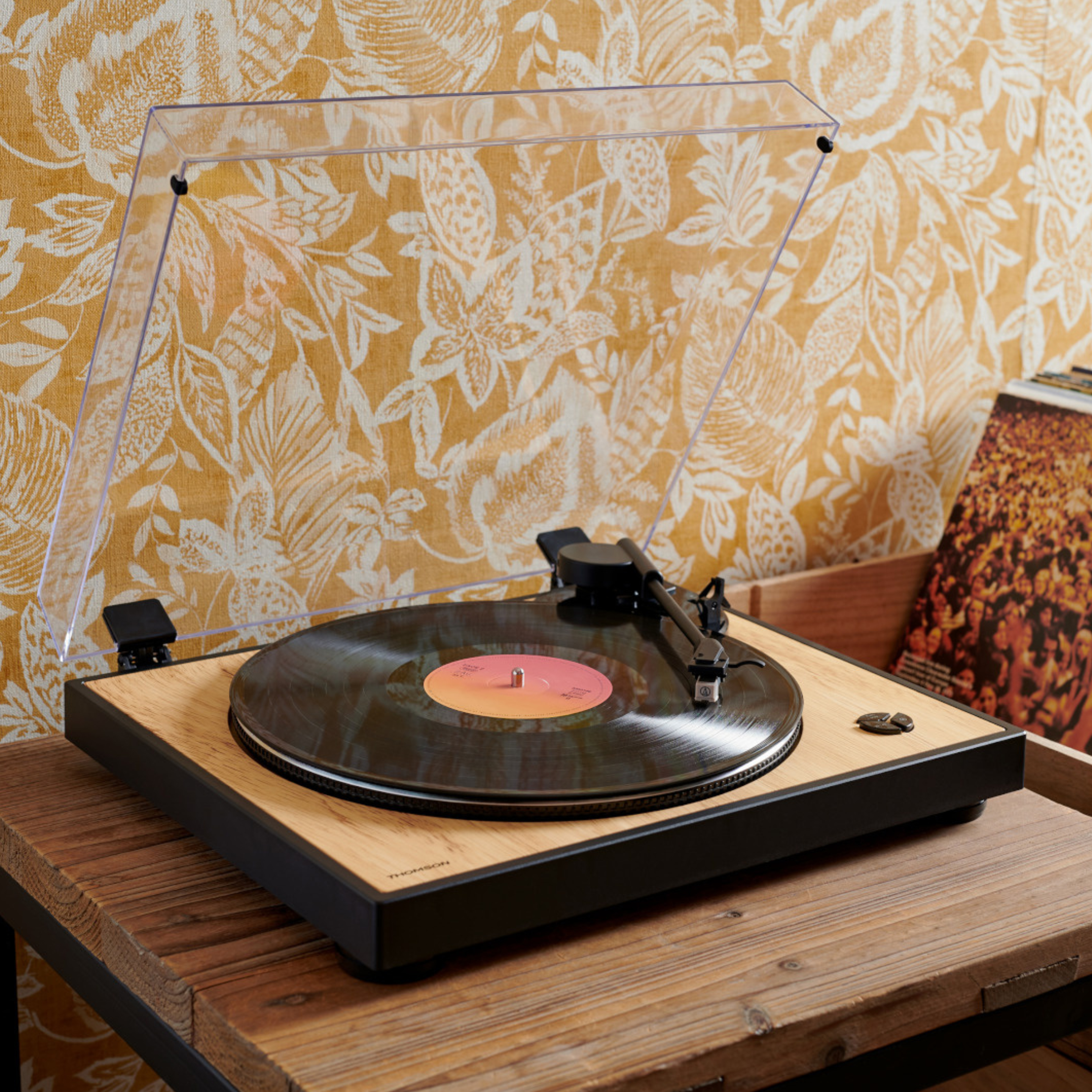 Gramofon z przezroczystą pokrywą na drewnianym stole z żółtym kwiatowym tłem tapety.