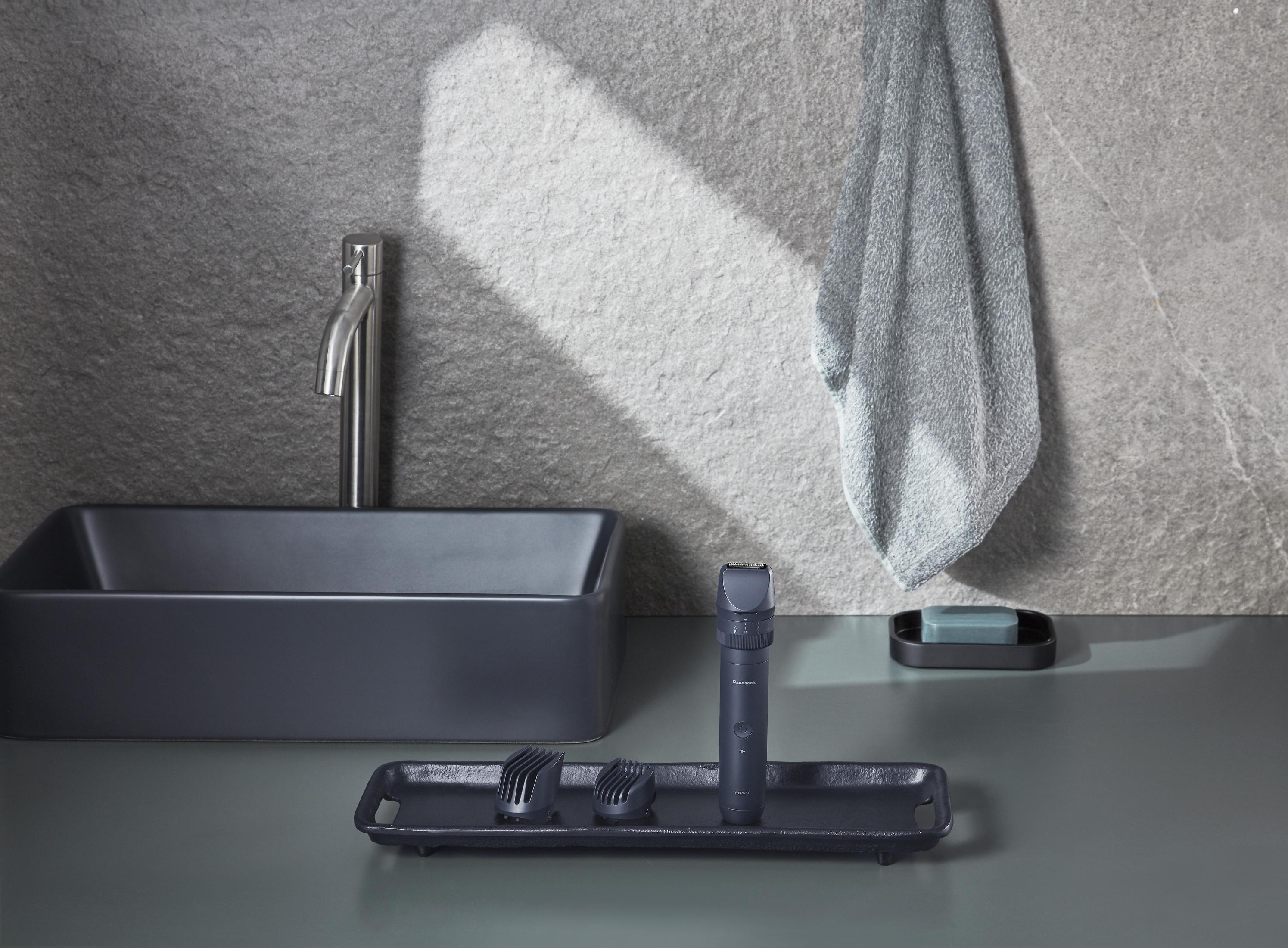 Scena w łazience z umywalką, lustrem i przyborami do pielęgnacji na tacy, z szarym ręcznikiem.