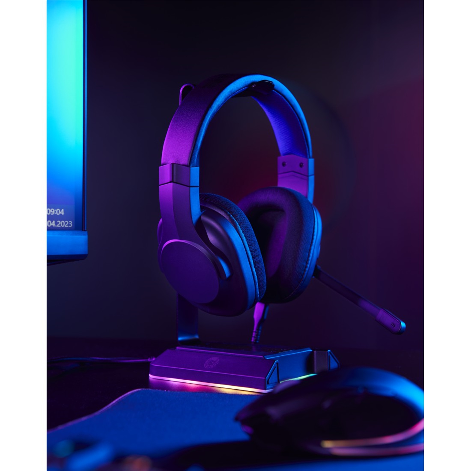 Cuffie da gioco su un supporto, illuminate da luci viola e blu. Un mouse in primo piano.