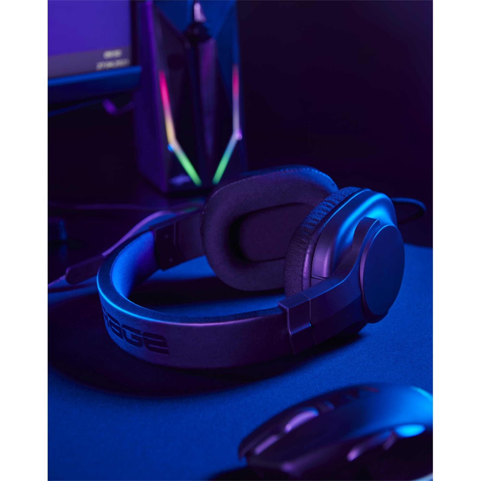 Cuffie da gioco nere su una superficie scura con un mouse e un monitor del computer sullo sfondo.