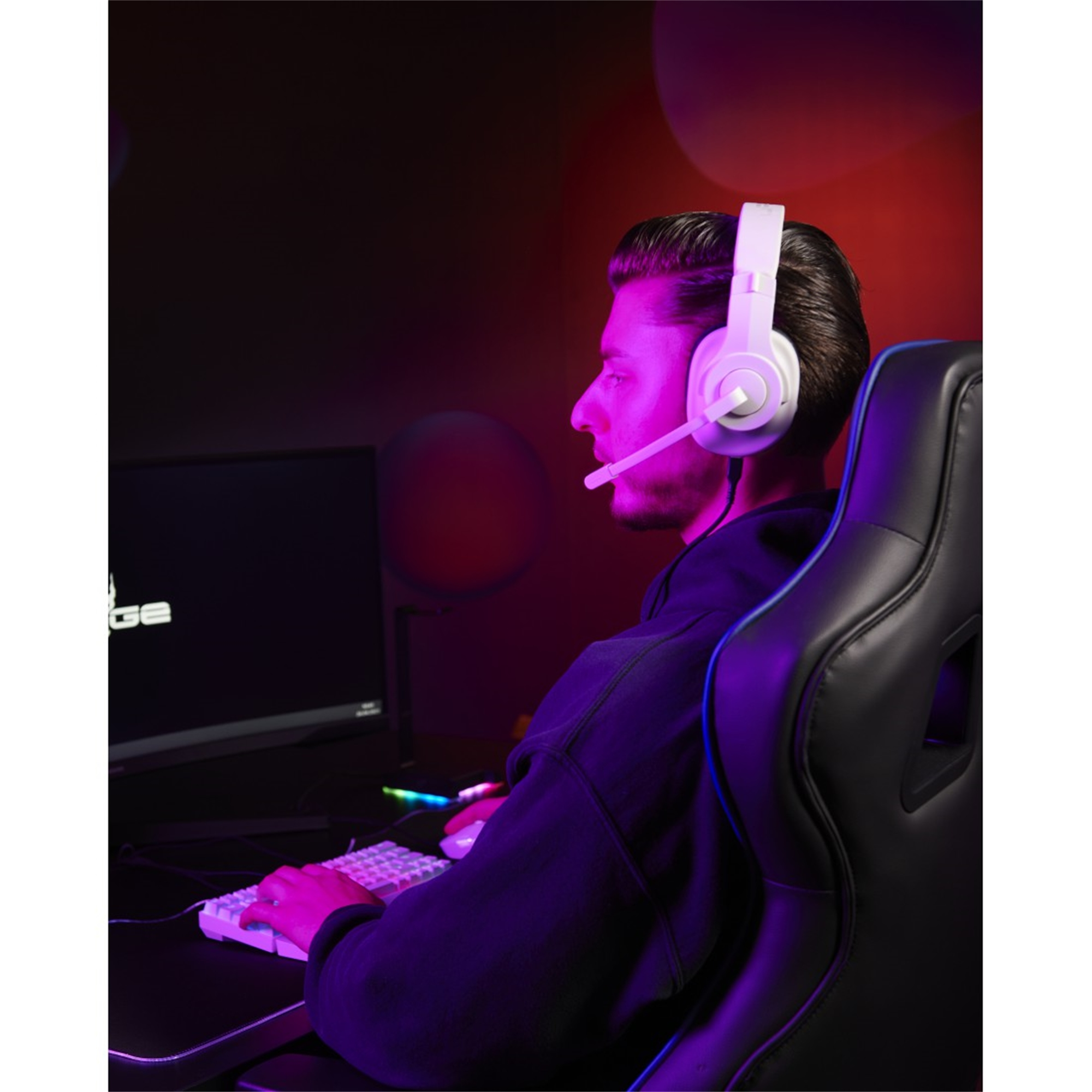 Mann mit Kopfhörern, spielt. Schwarzer Stuhl, weiße Tastatur, Monitor im Hintergrund. Dunkler Raum.