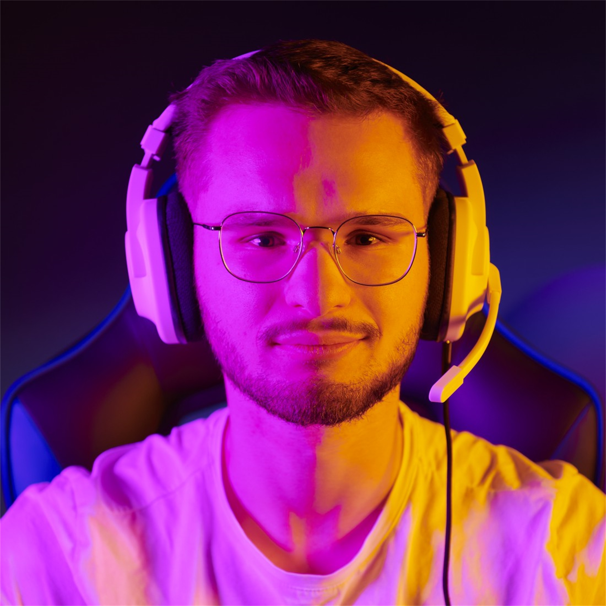 Mann mit Brille und Kopfhörern, beleuchtet mit rosa und gelben Lichtern. Dunkler Hintergrund.