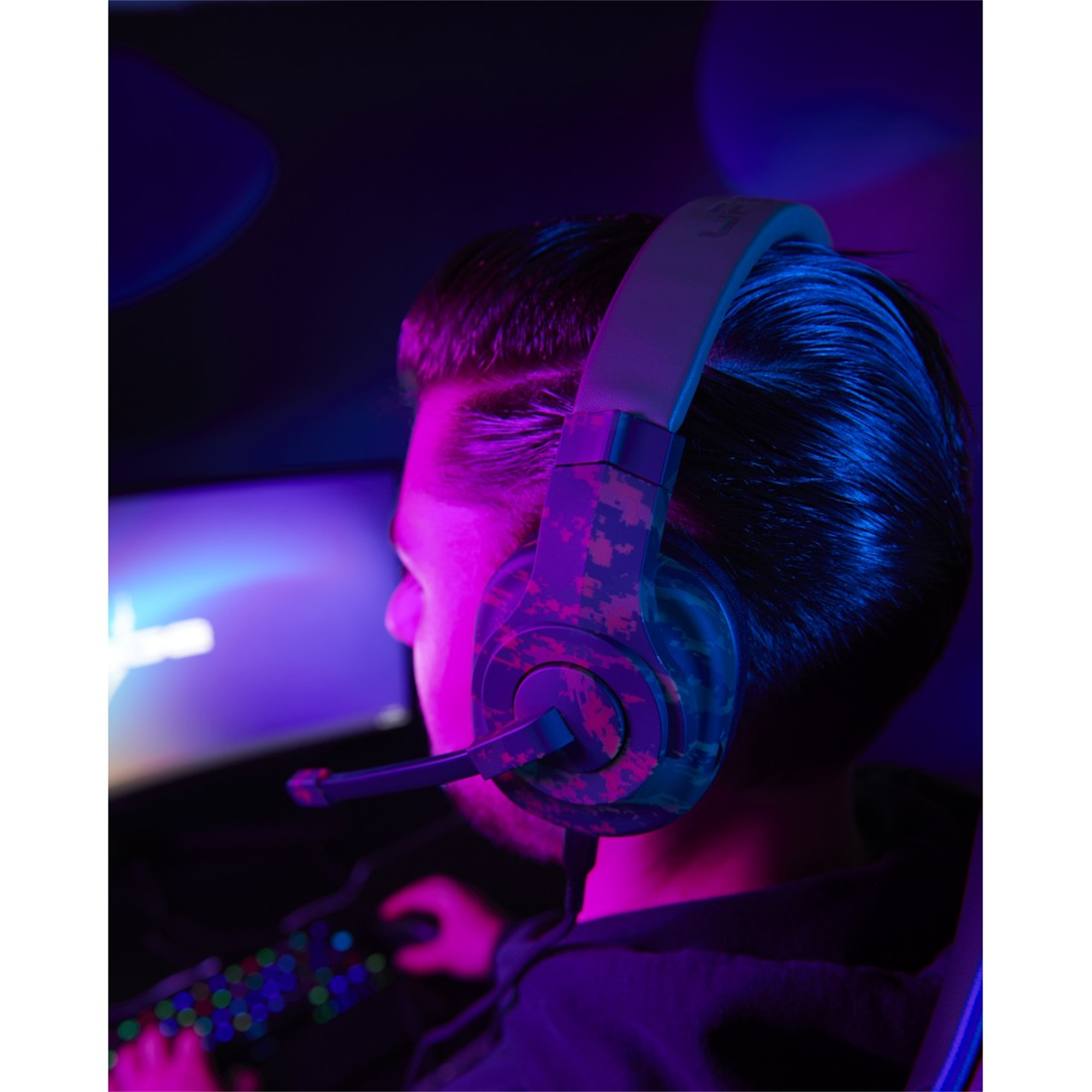 Eine Person mit einem Gaming-Headset mit Mikrofon, in einem schwach beleuchteten Raum mit einem Monitor.