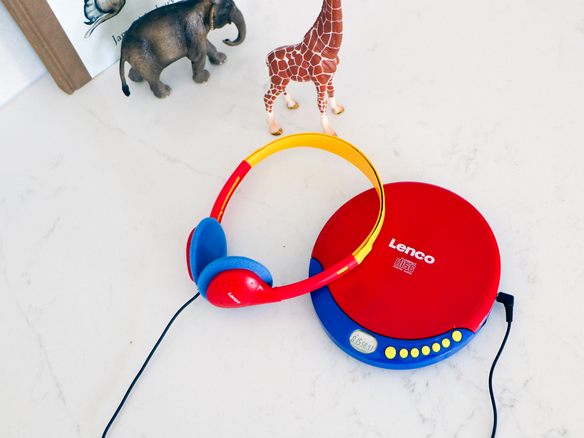 Roter und blauer Lenco CD-Player mit Kopfhörern und Spielzeugtieren auf weißer Oberfläche.
