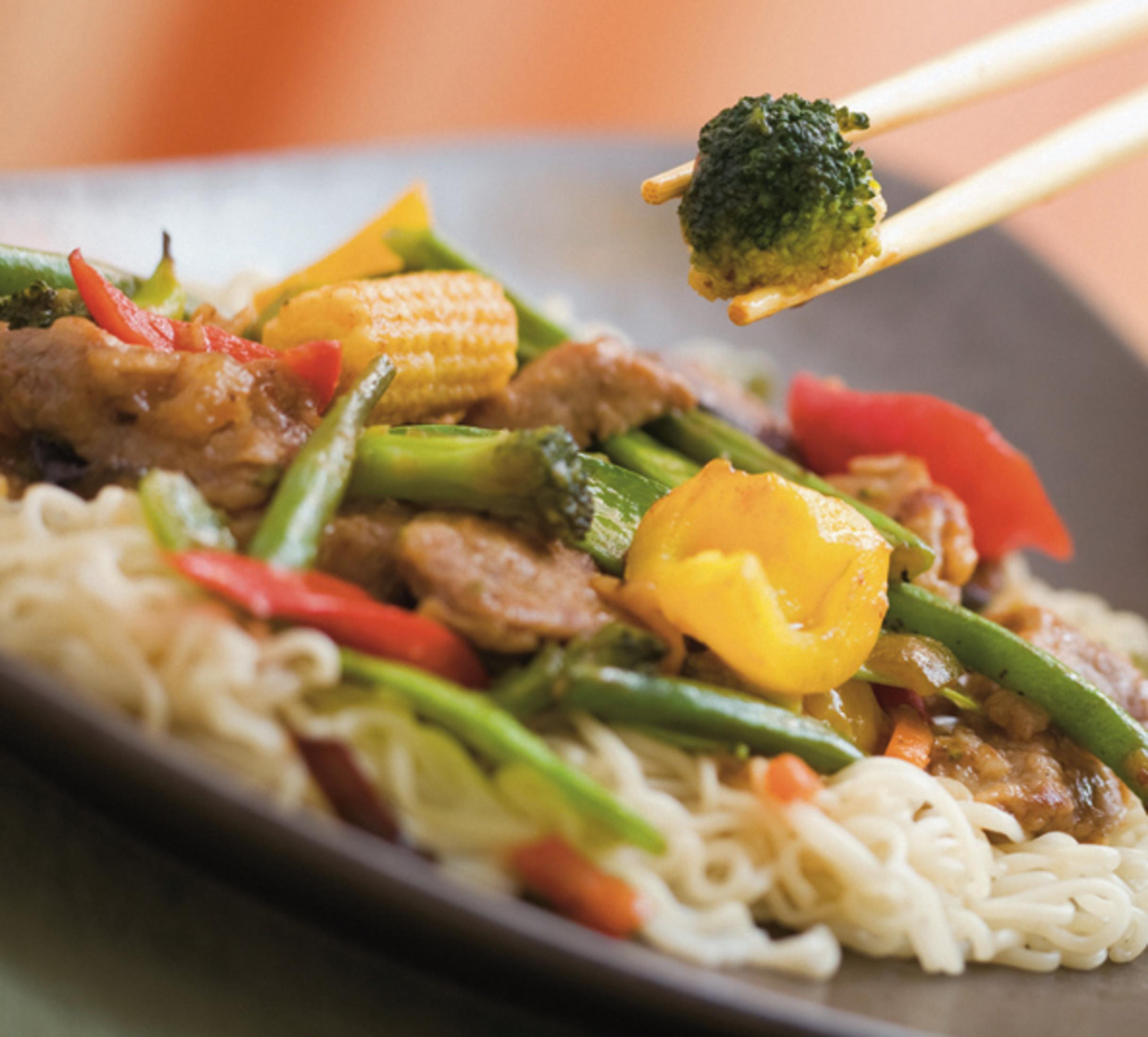 Piatto di noodles con carne, broccoli, peperoni e mais. Bacchette prendono broccoli.