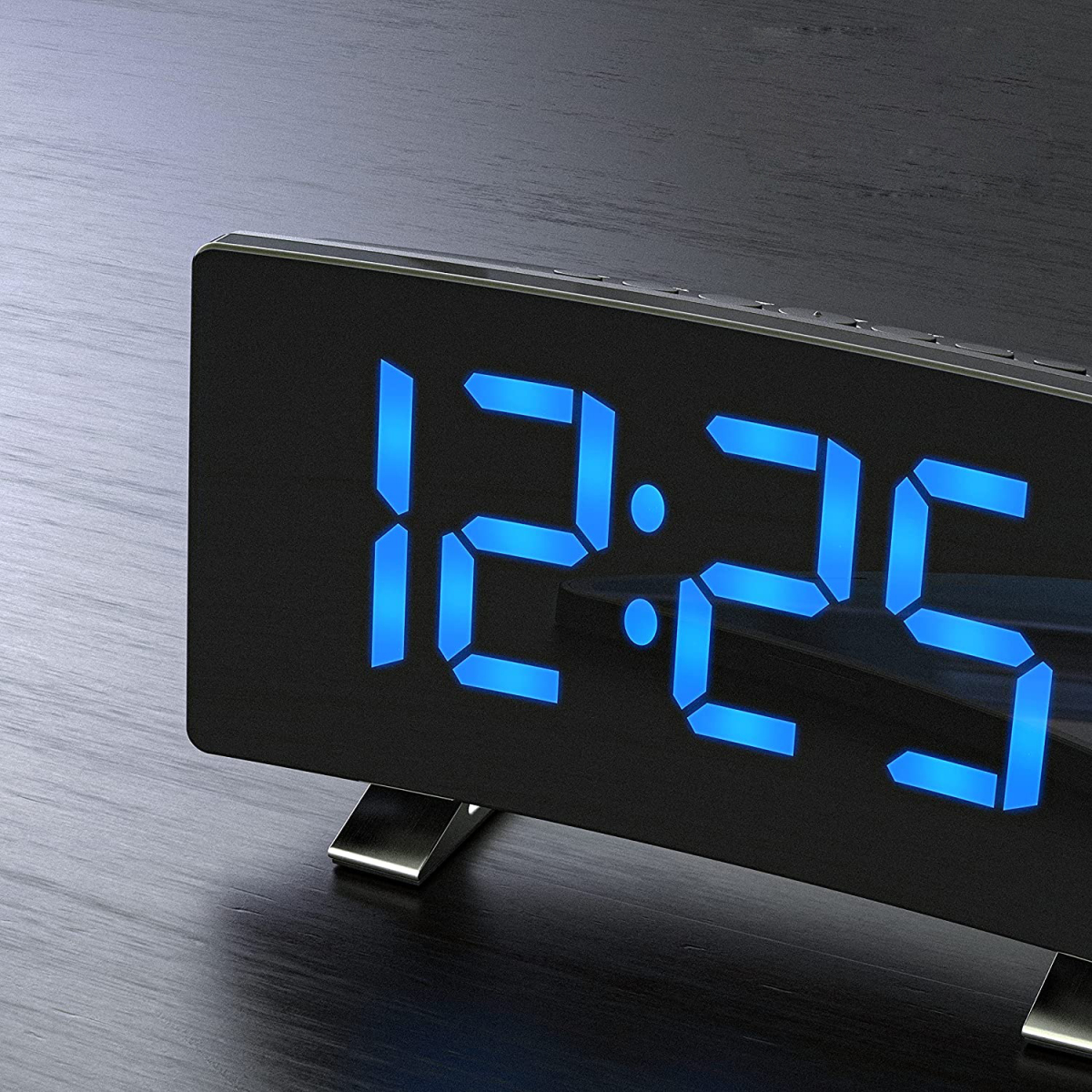 Schwarze Digitaluhr mit blauen Ziffern, die 12:25 anzeigt. Auf dunkler Holzoberfläche.