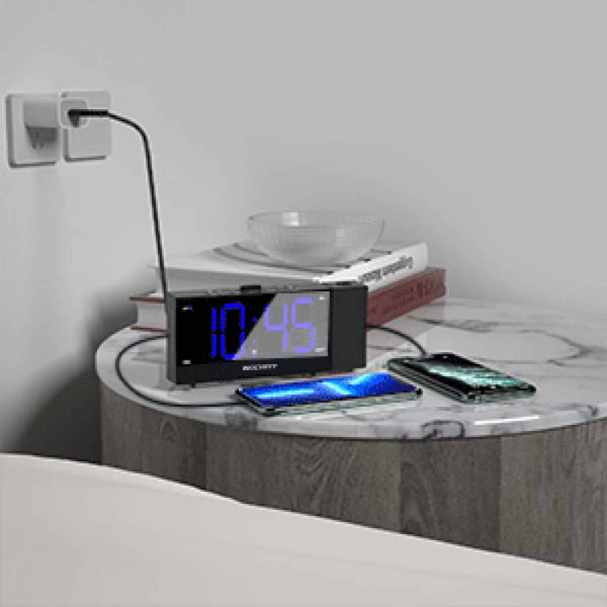 Schwarzer Wecker mit blauer Digitalanzeige 10:45. Zwei Telefone und eine Schüssel auf dem Tisch.