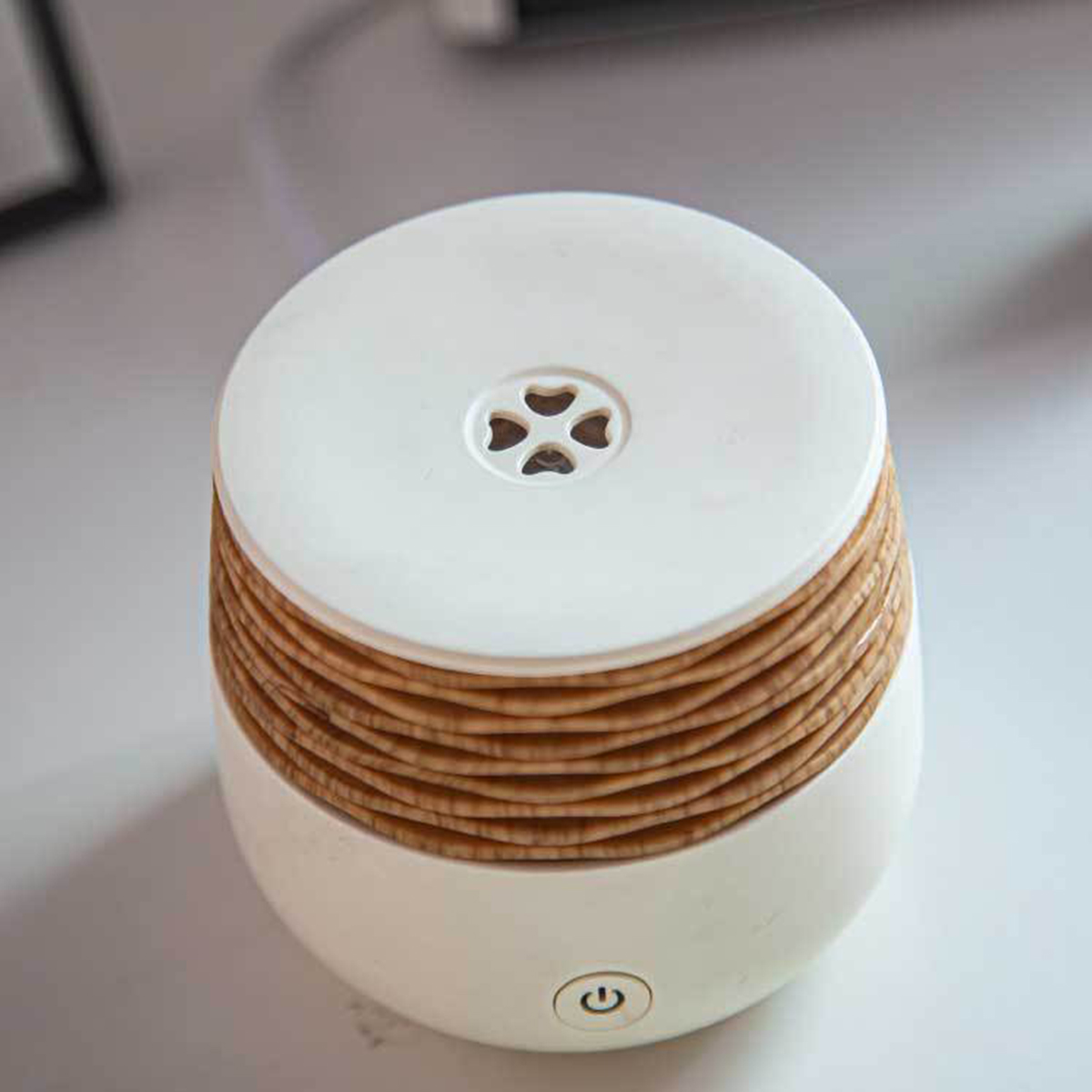 Ein weißer und holzmaserter Diffusor für ätherische Öle, mit einem Einschaltknopf vorne.