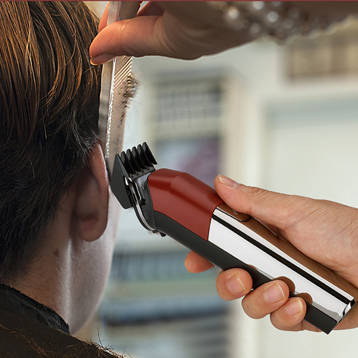 Eine Person schneidet mit einem elektrischen Haarschneider die Haare einer anderen Person. Der Clipper ist rot und schwarz.