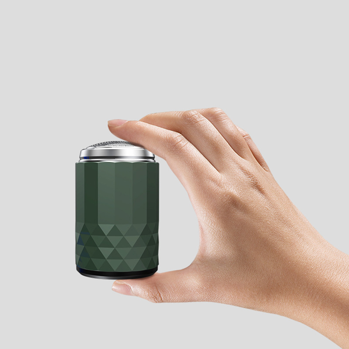 Grüner zylindrischer Elektrorasierer in einer Hand. Eine Hand hält den Rasierer. Grauer Hintergrund.