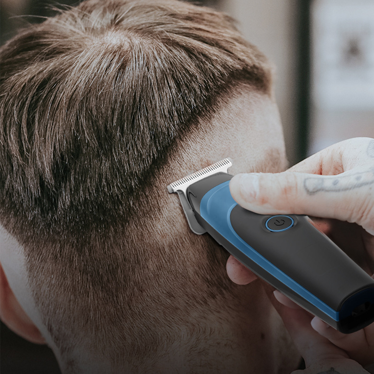 Die Hand einer Person, die einen schwarz-blauen Haarschneider auf dem Hinterkopf eines Mannes benutzt.