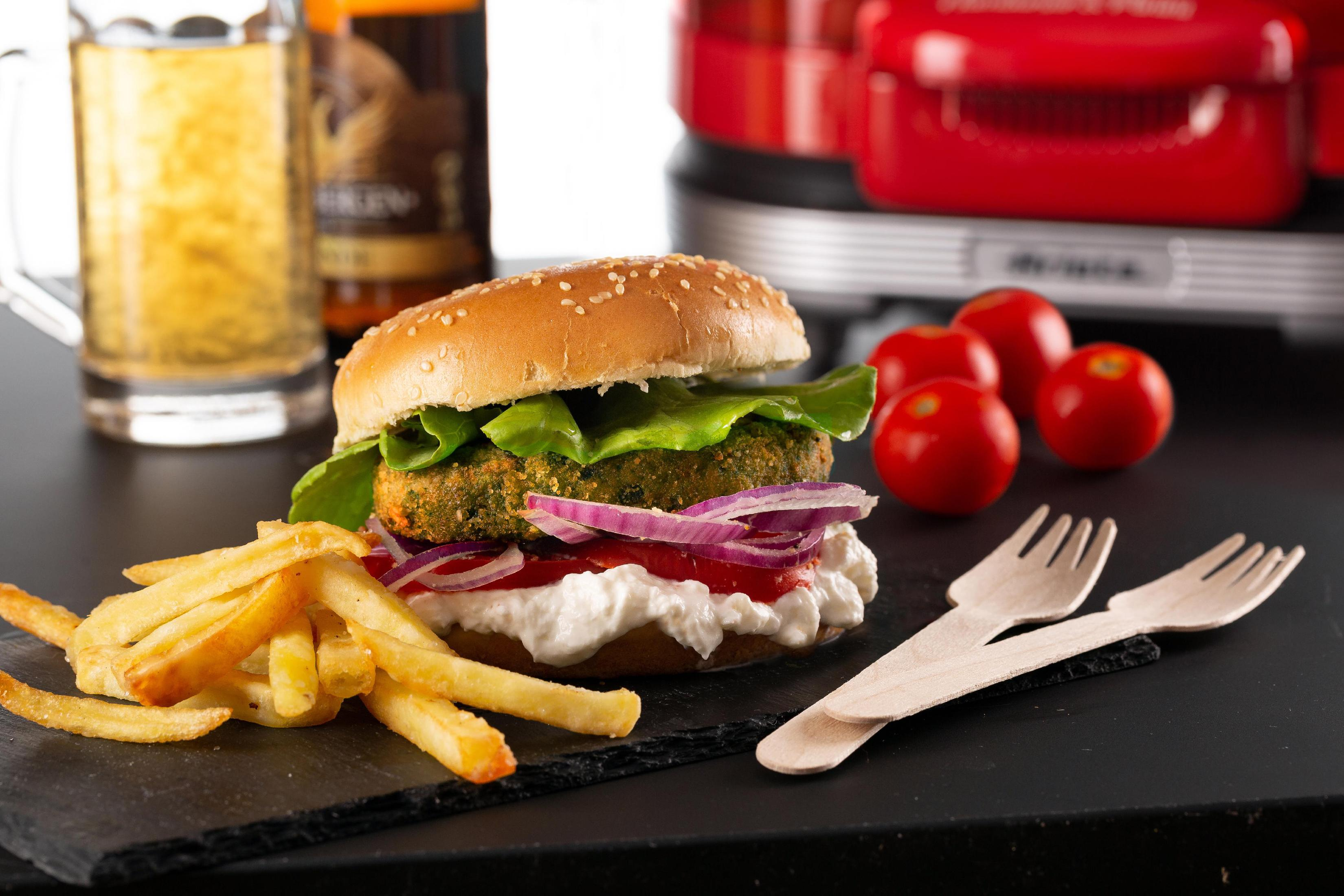 Burger mit Pommes, Tomaten und Bier. Der Burger hat Salat, Tomate und Patty.