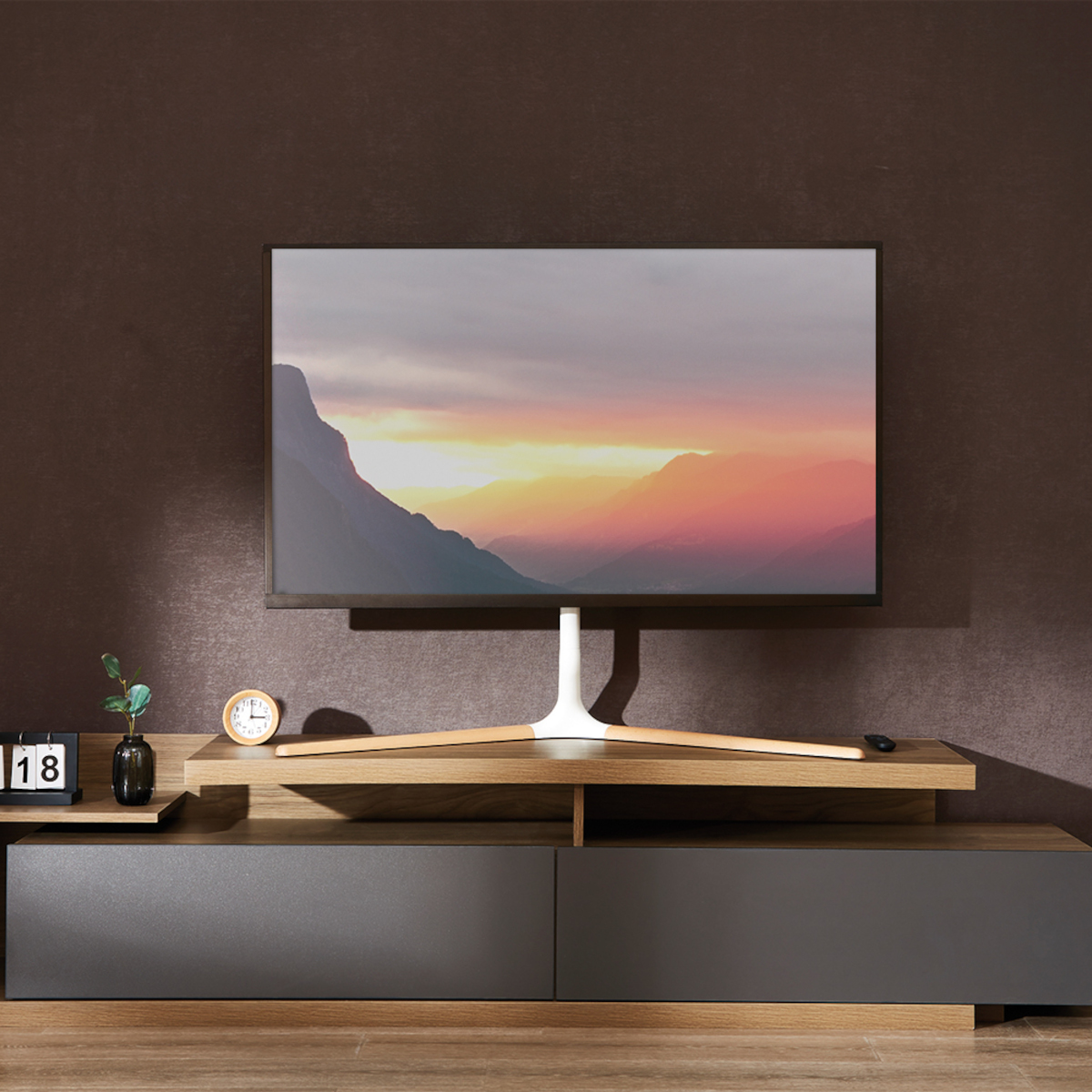 Ein moderner Fernseher auf einem Holzständer vor einer braunen Wand. Eine Uhr und ein Kalender stehen da.