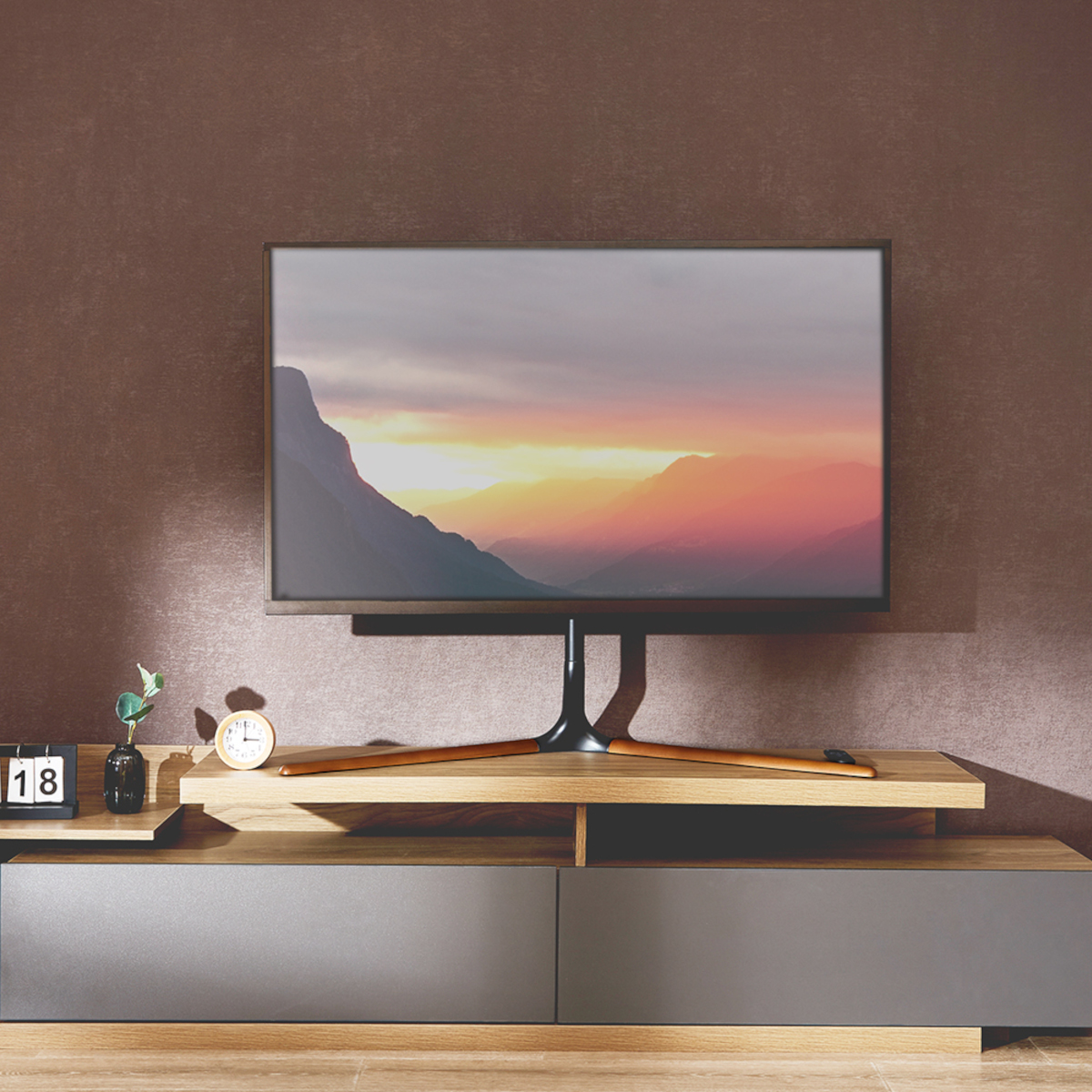 Fernseher auf einem Holzständer, mit einer Sonnenuntergangslandschaft, vor einer braunen Wand.
