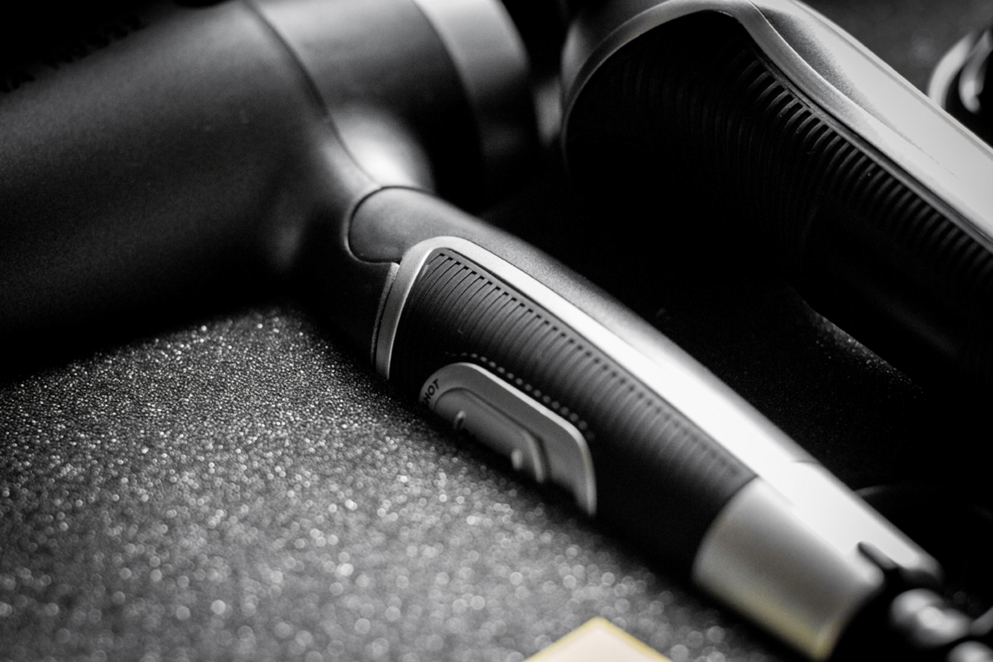 Close-up of a black hair dryer with a silver detail. Dark background.