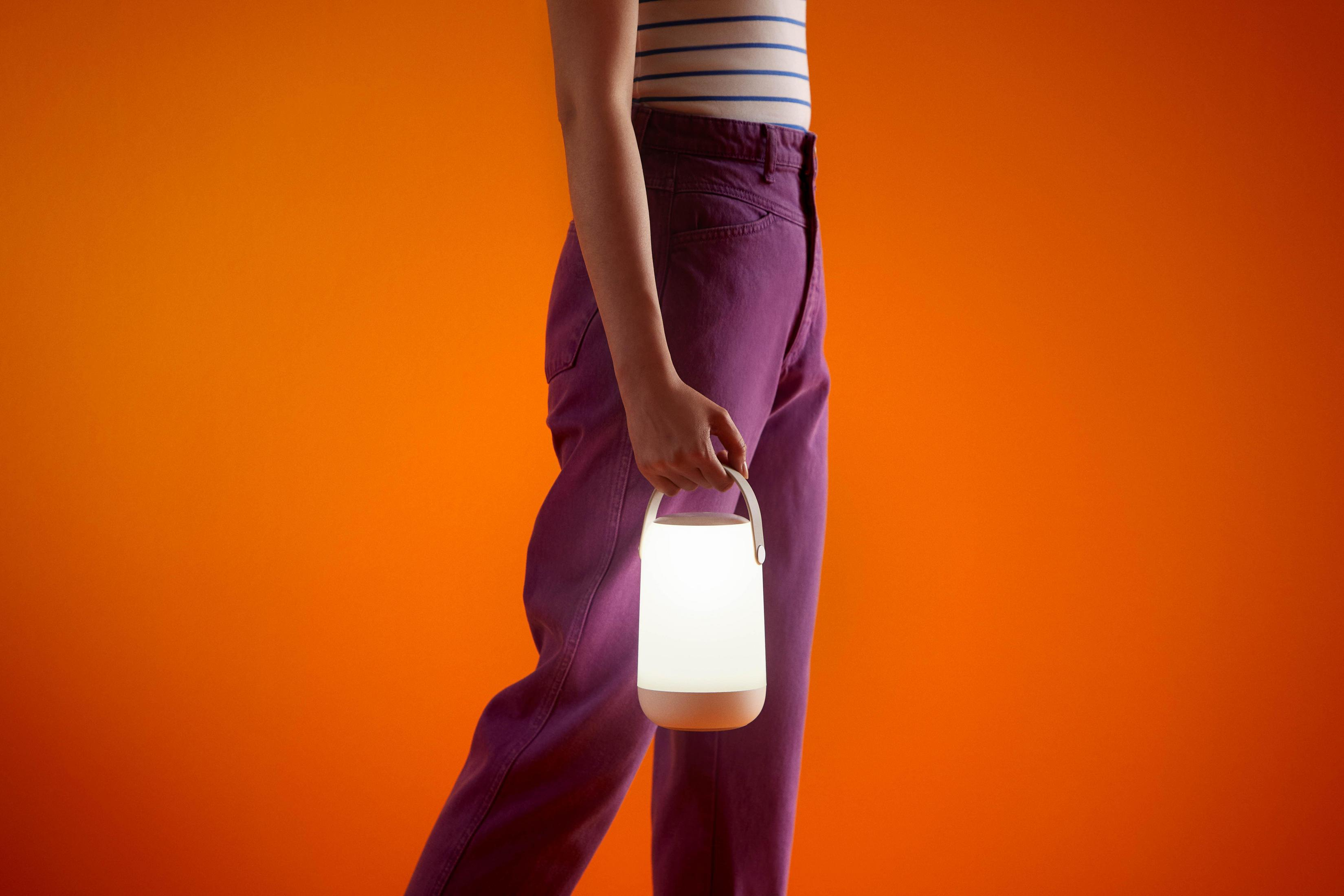 Persoon die een gloeiende, witte, cilindrische lantaarn vasthoudt. Draagt paarse broek, oranje achtergrond.
