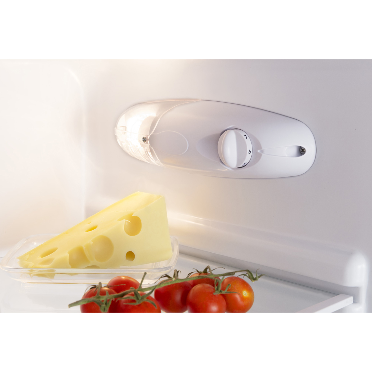 Ein Kühlschrankinnenraum mit Käse, Tomaten und einer Leuchte. Das Licht ist an und beleuchtet das Essen.