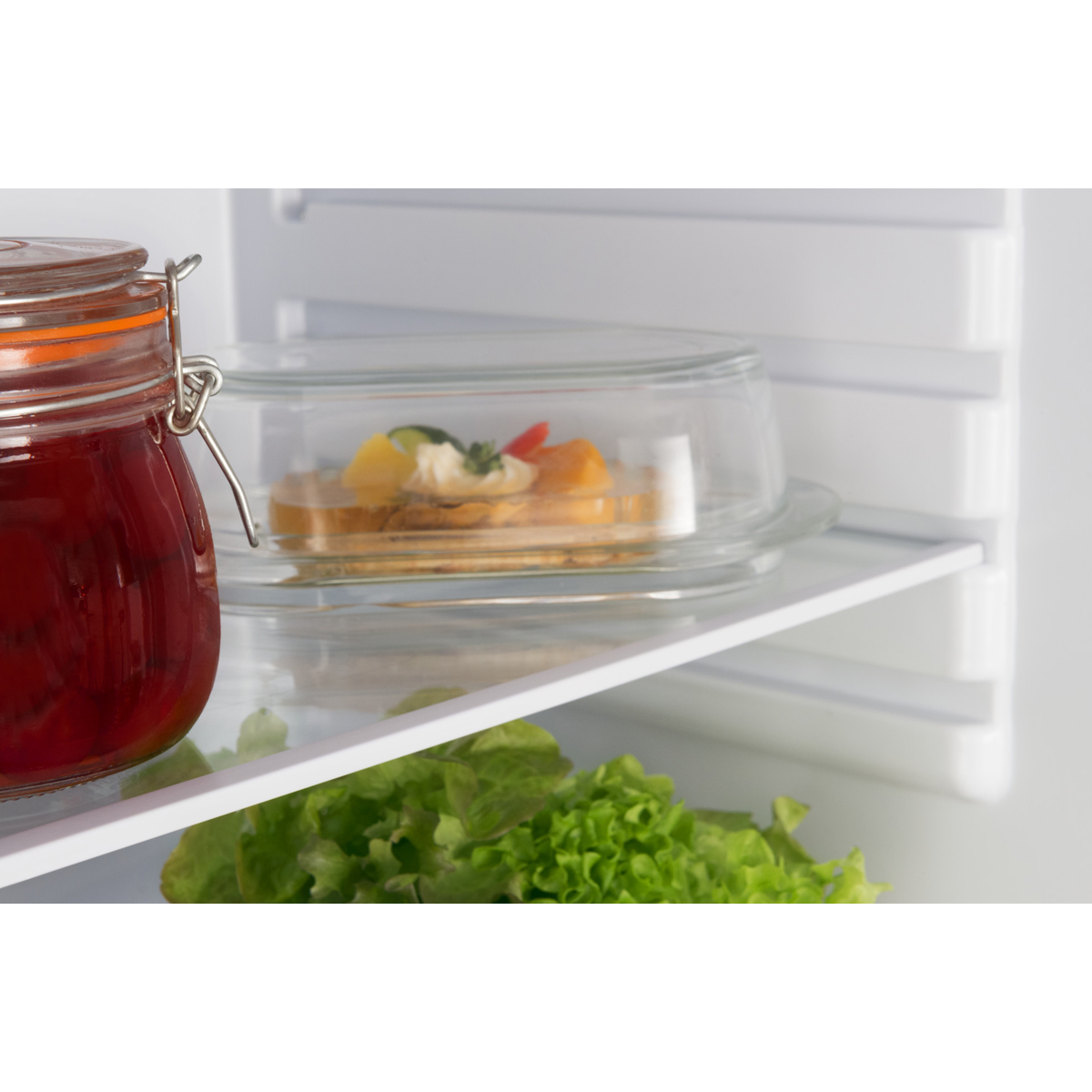 Kühlschrankregal mit einem Glas, einem Glasbehälter mit Essen und Salat.