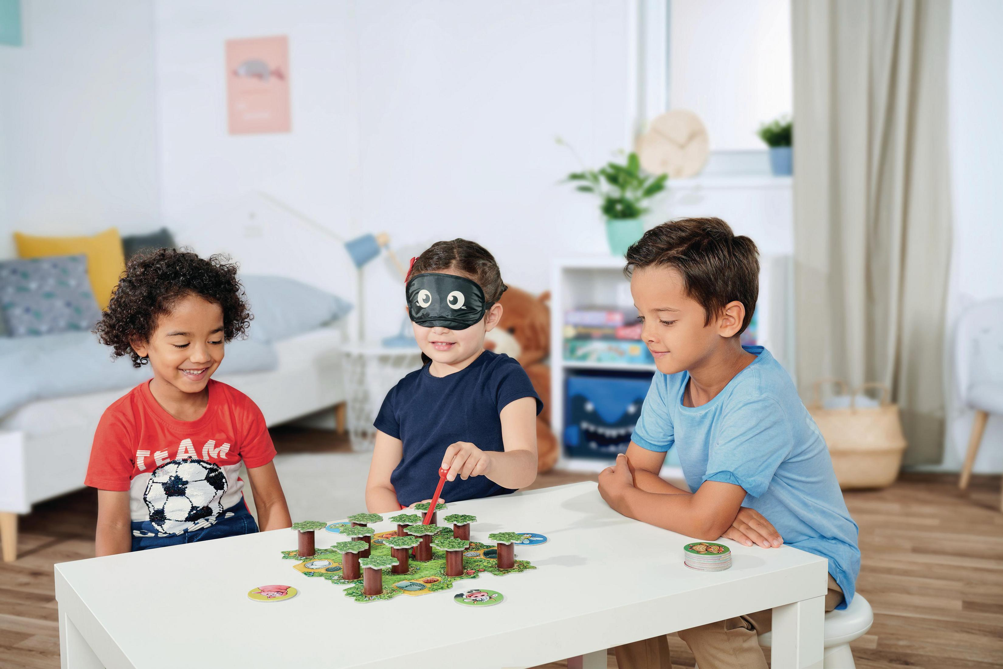 Drei Kinder spielen ein Brettspiel. Eines ist mit verbundenen Augen, das Spiel ist auf dem Tisch.