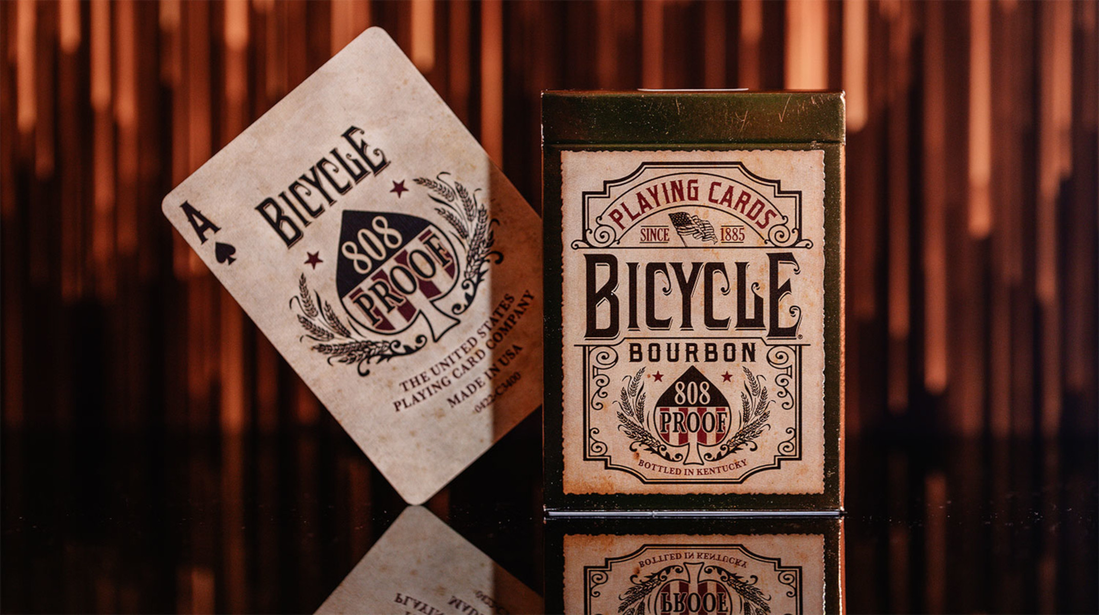 Spielkarte, Pik-Ass, und ein Bicycle Bourbon Kartenspiel liegen auf glänzender Oberfläche, brauner Hintergrund.