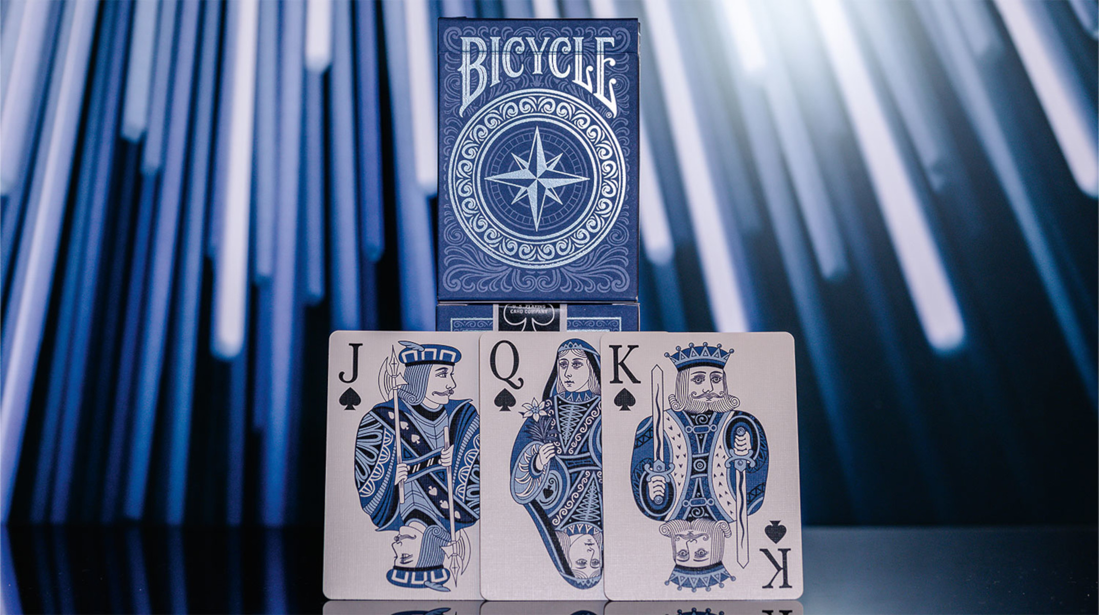 Vier Spielkarten: Bube, Dame und König von Pik, und eine Bicycle-Kartenspielbox. Blau und Weiß.