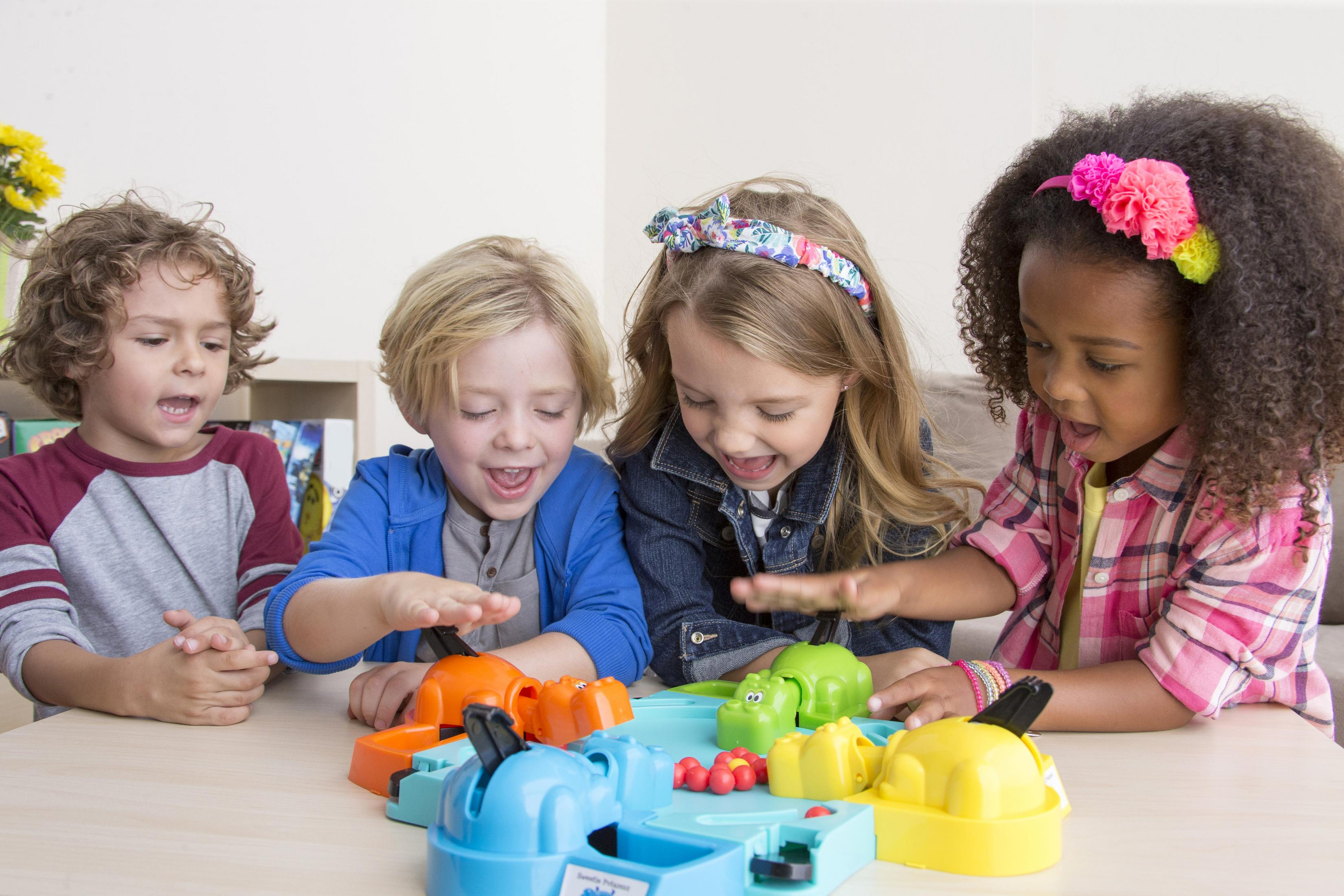 Vier Kinder spielen Hungry Hungry Hippos. Das Spiel hat orange, grüne und gelbe Flusspferde.