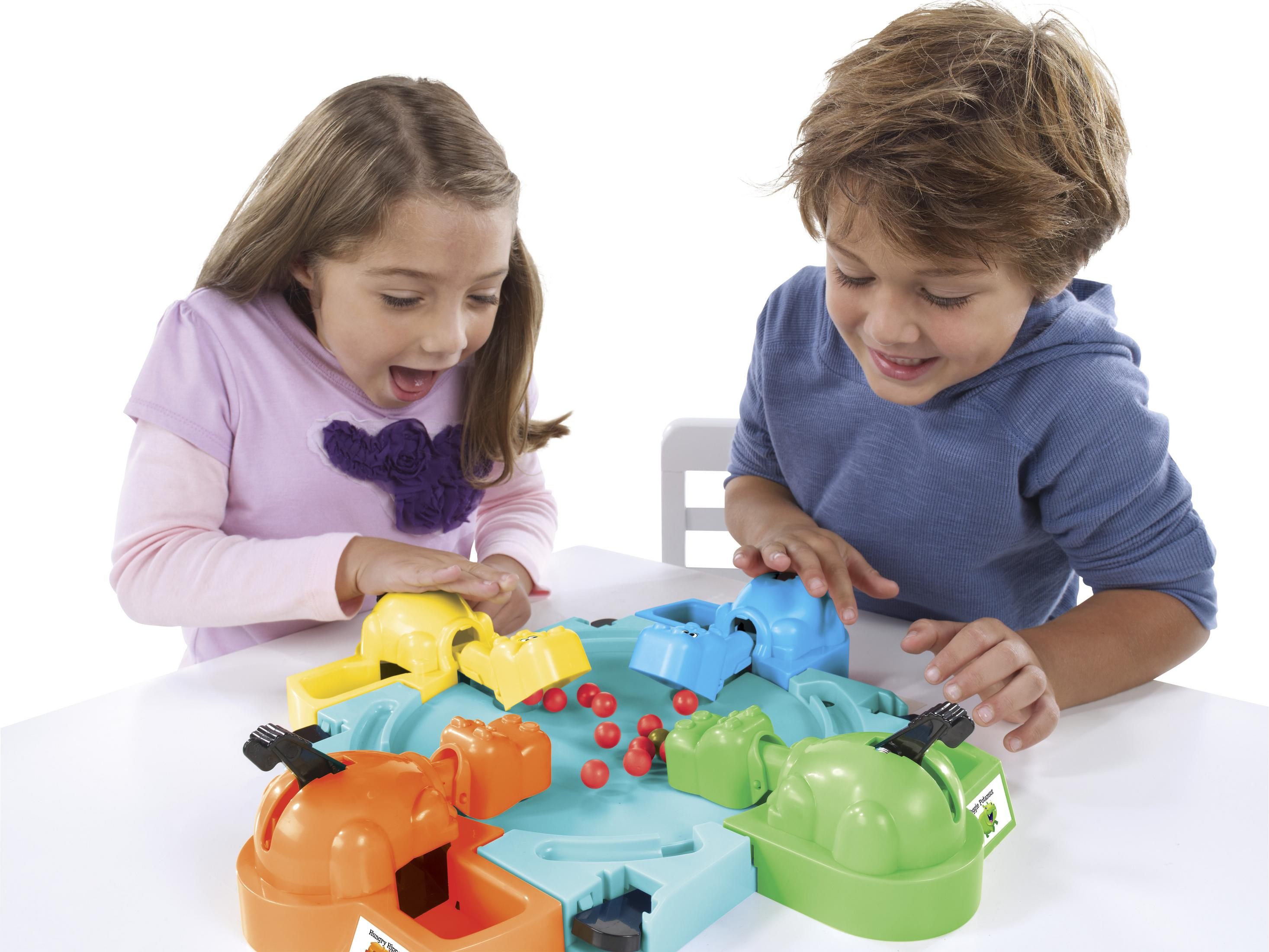 Zwei Kinder spielen ein Spiel mit bunten Flusspferden und roten Kugeln auf einem weißen Tisch.