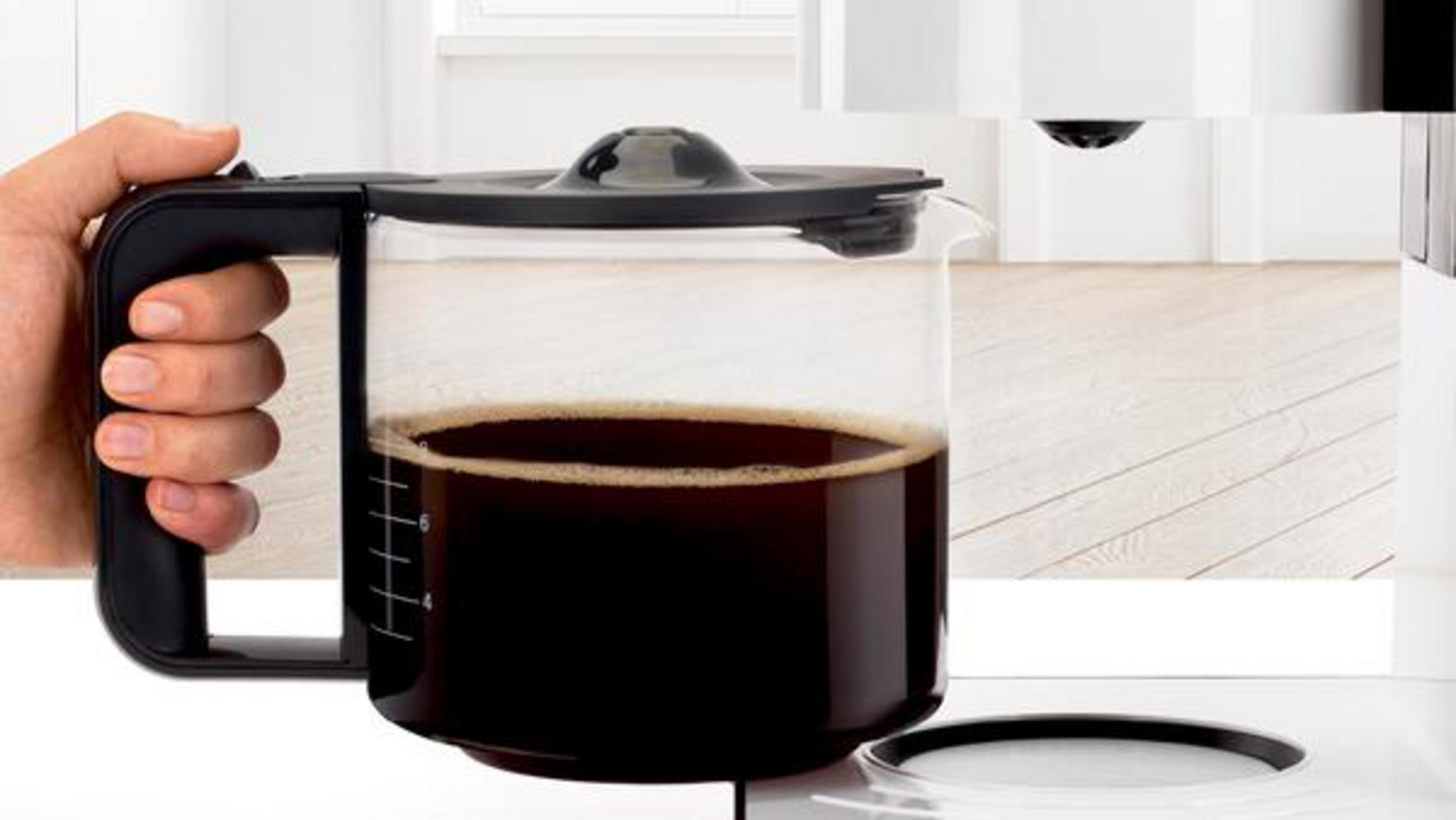 Ręka trzyma szklany dzbanek do kawy wypełniony ciemną kawą.