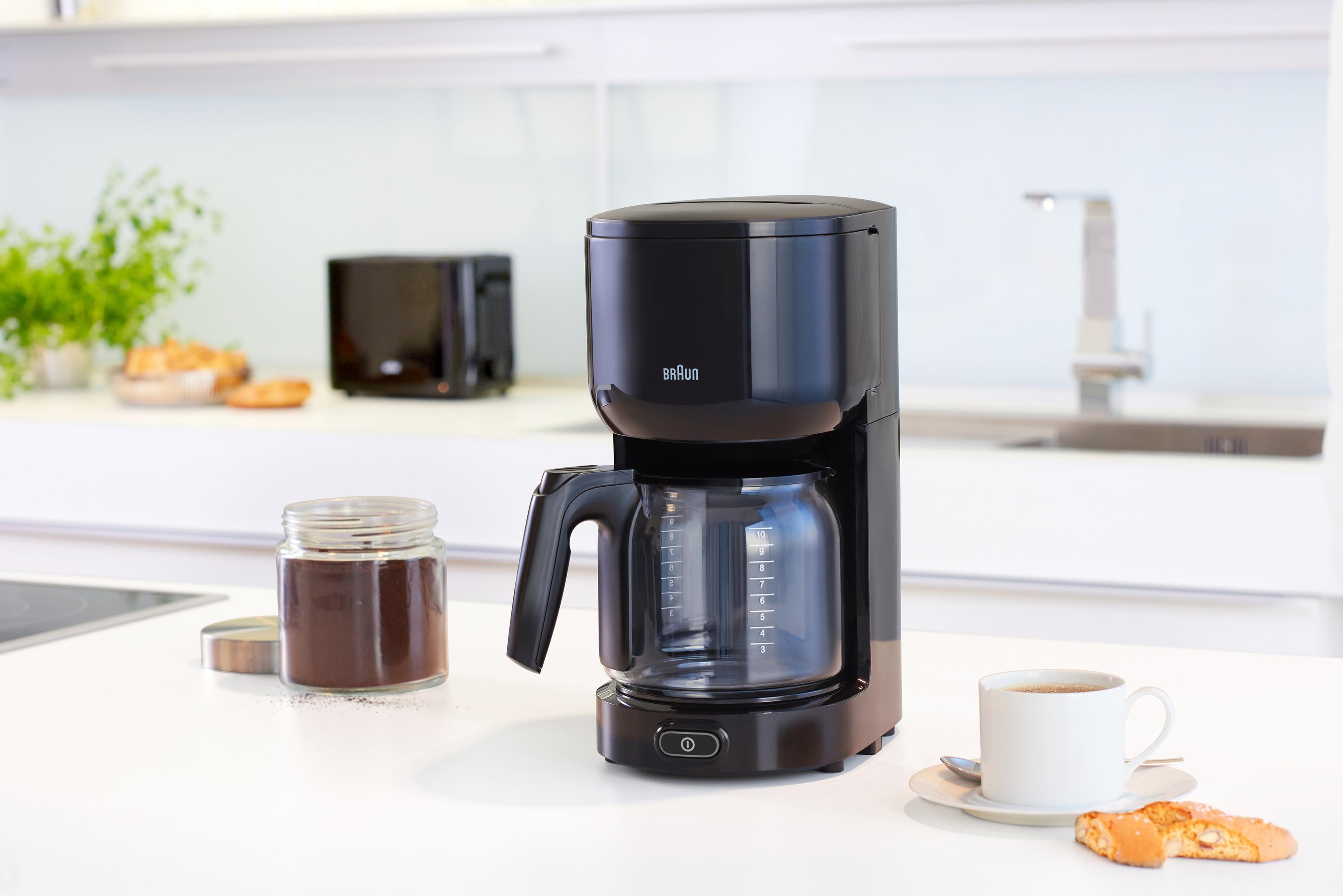 Czarny ekspres do kawy, słoik mielonej kawy, filiżanka kawy i toster na białym blacie.