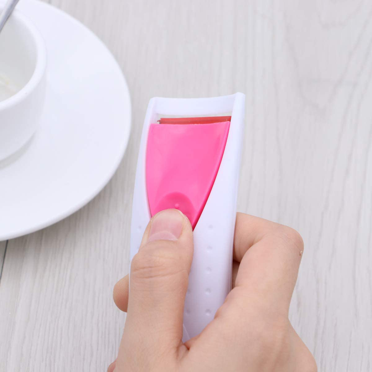 Die Hand einer Person, die einen rosa-weißen Wimpernzange hält.