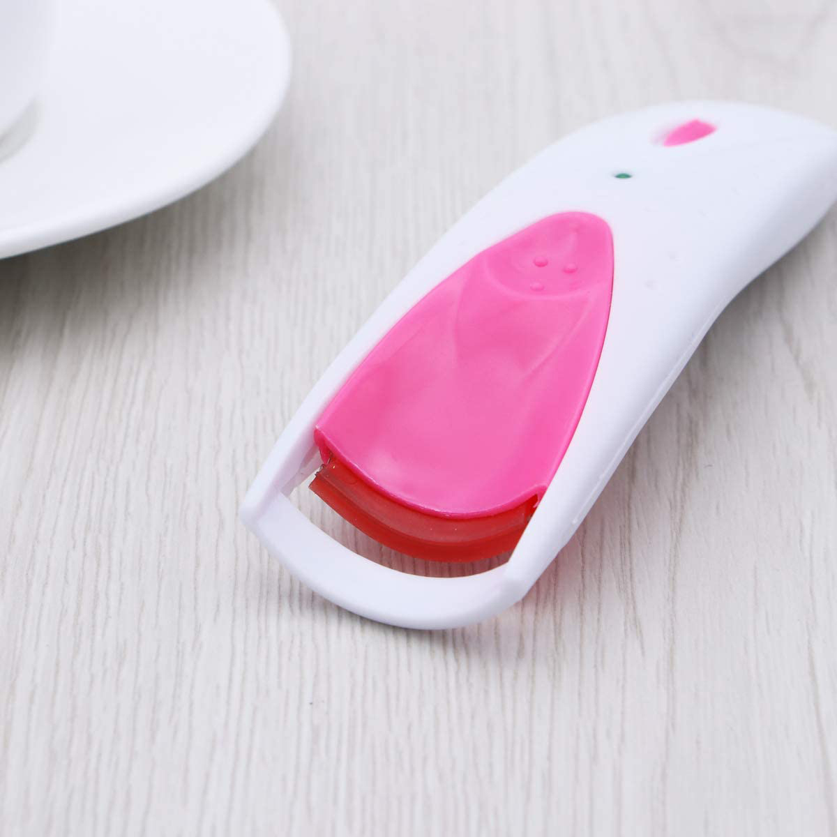Elektrische Wimpernzange in Weiß und Pink, mit einem kleinen pinken Knopf und einer weißen Oberfläche.