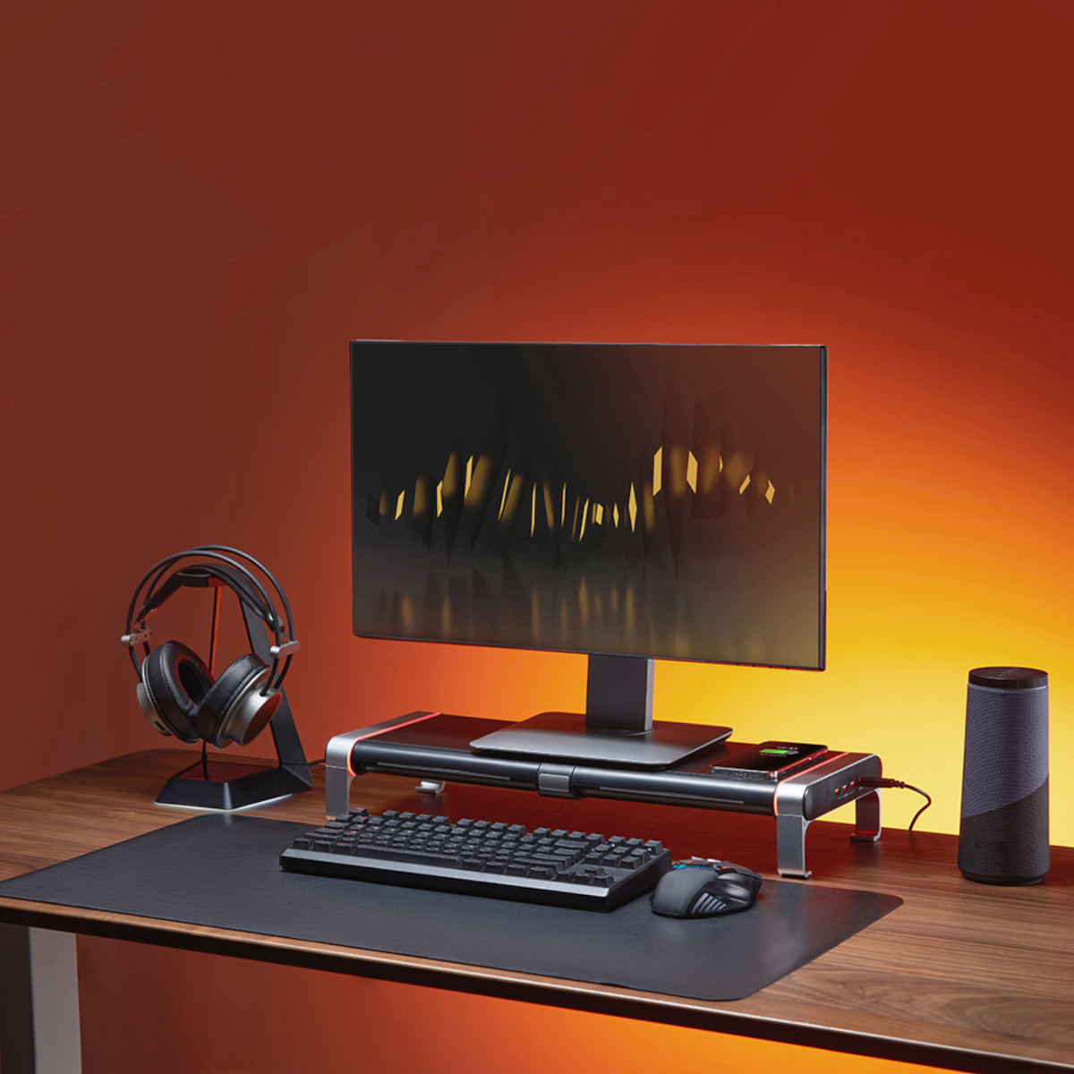 Ein Computer-Setup mit Monitor auf einem Ständer, Kopfhörern, Tastatur, Maus und Lautsprecher auf einem Holztisch.