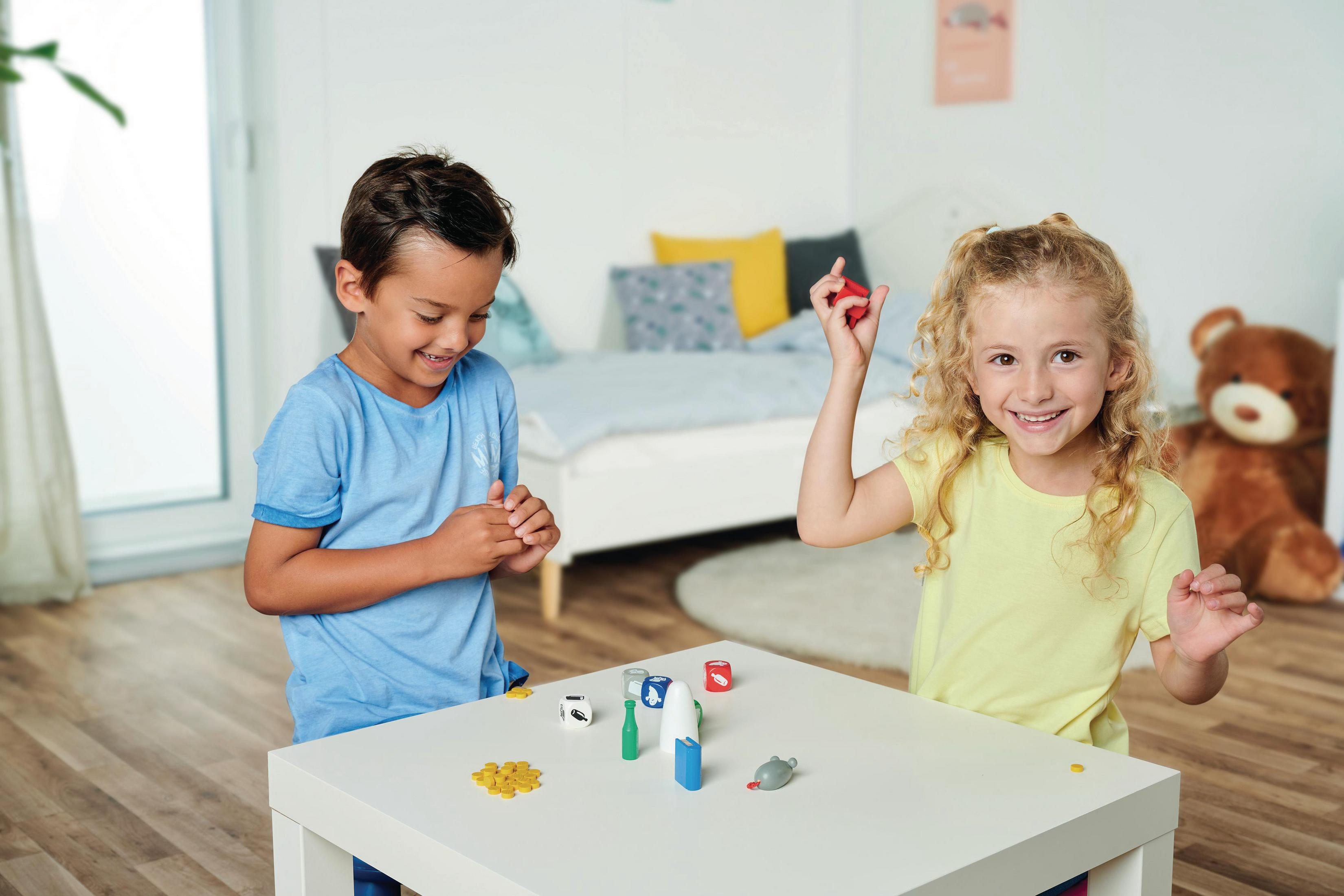 Zwei Kinder spielen ein Brettspiel mit Würfeln und roten, weißen und blauen Spielsteinen.