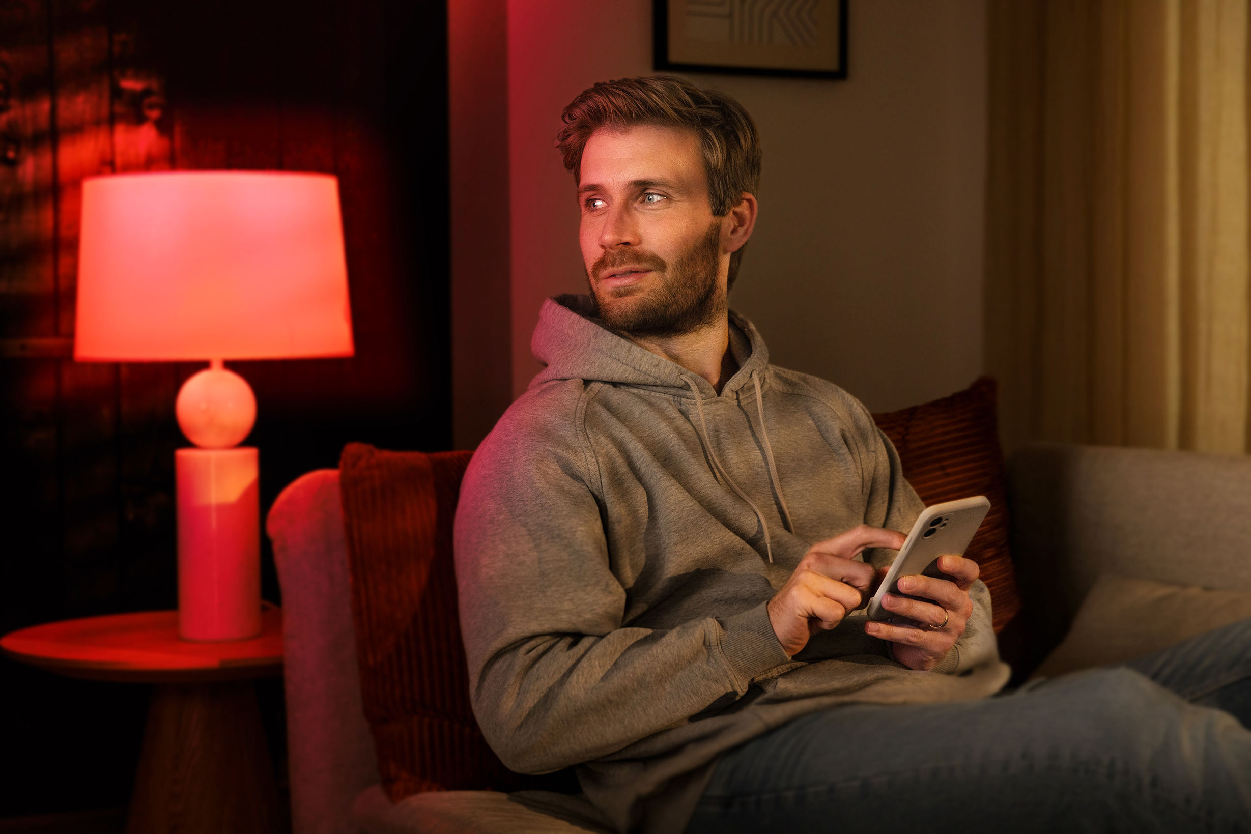 Ein Mann sitzt auf einem Sofa, schaut weg und hält ein Telefon. Eine Lampe ist an.