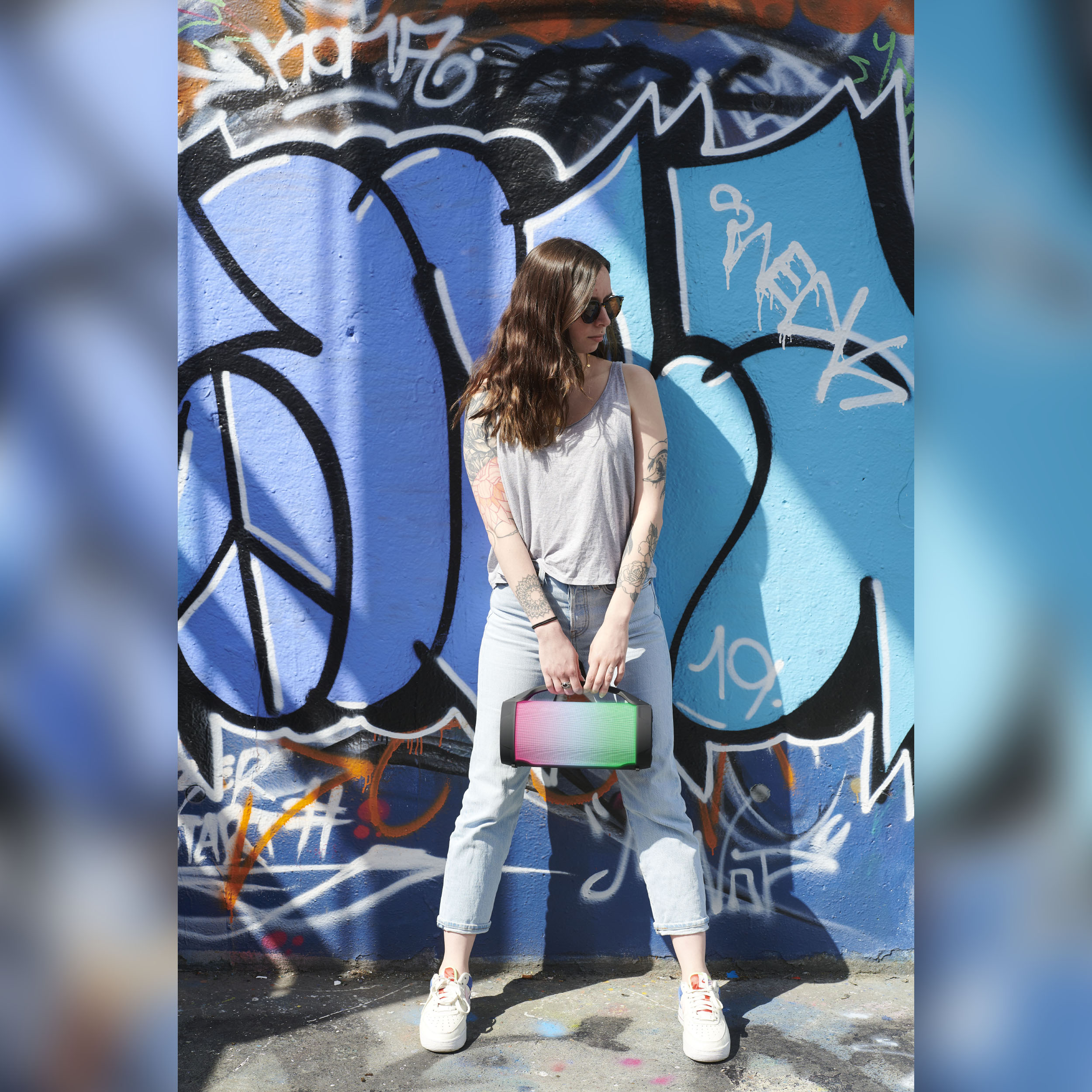 Kobieta stojąca przed ścianą graffiti, trzymająca kolorową torebkę.