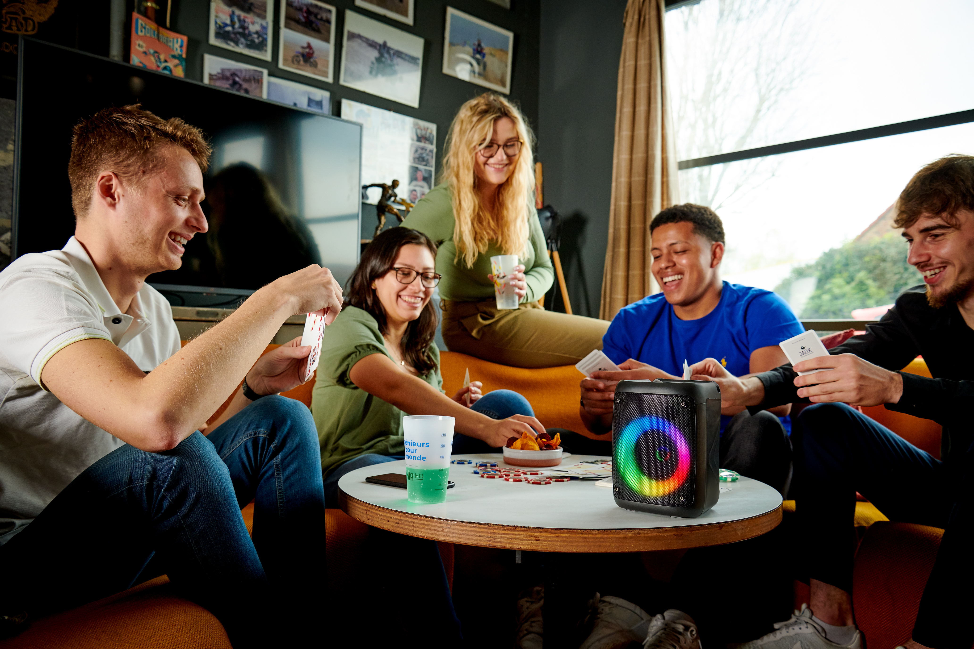 Grupa pięciu osób grających w karty i pijących. Głośnik na stole.