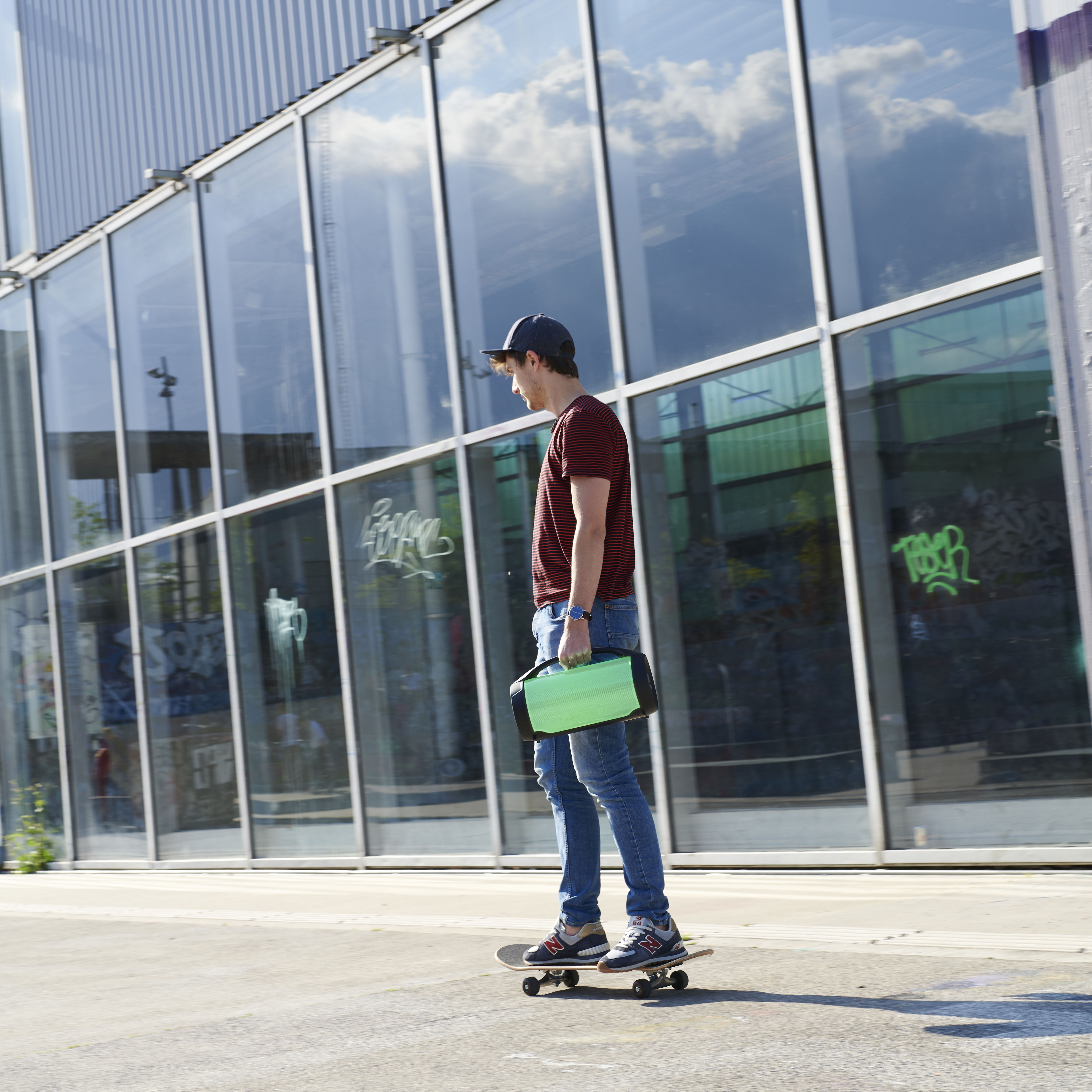 Mężczyzna jeździ na deskorolce, trzymając zielony głośnik.