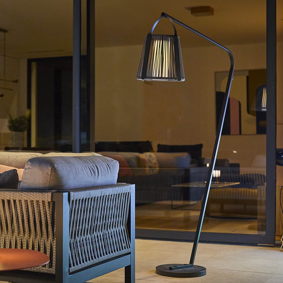 Schwarze Stehlampe mit gewebtem Schirm und Sofa im Hintergrund.