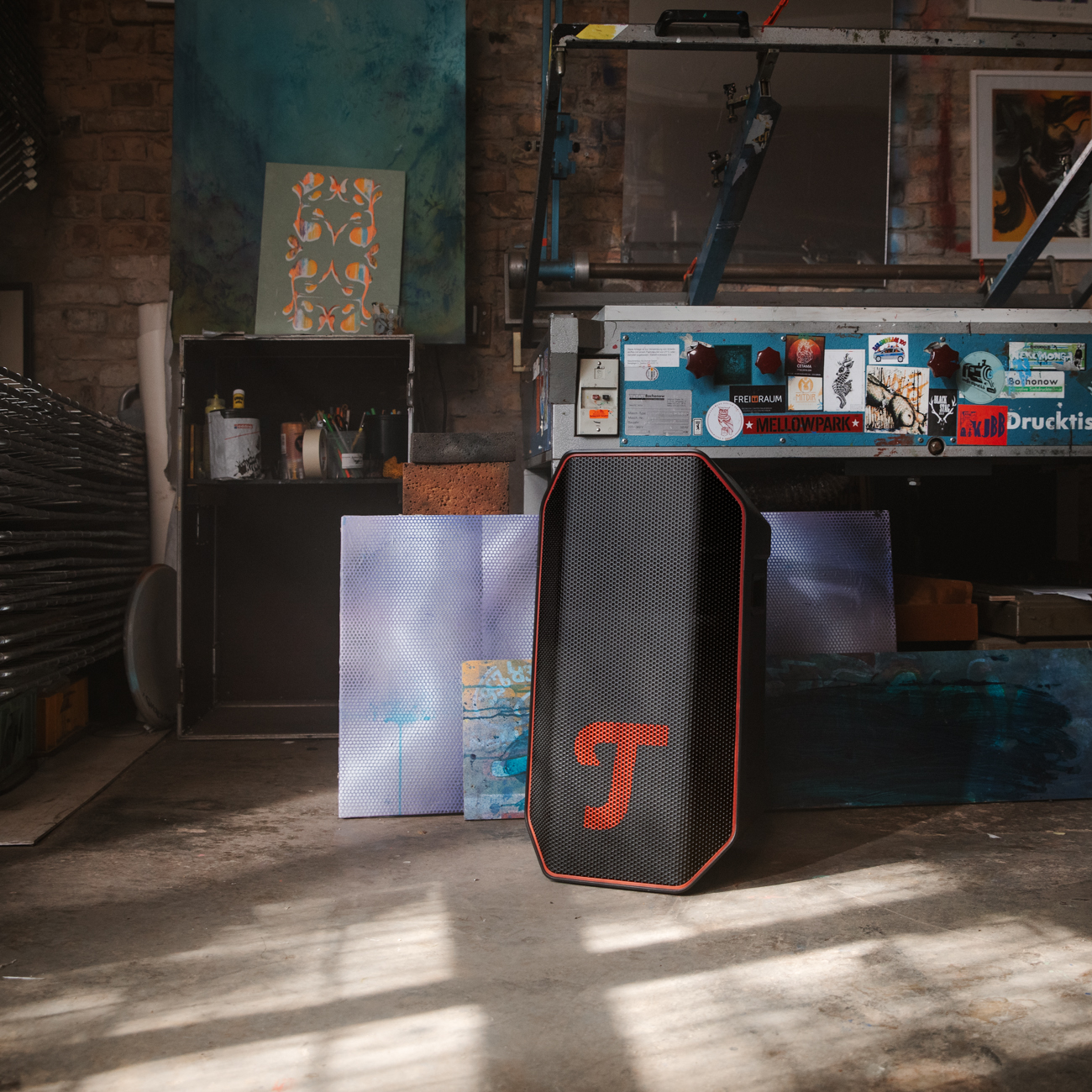 Ein schwarzer und roter Lautsprecher mit T-Logo in einem Studio. Im Hintergrund Malerei und Druckausrüstung.