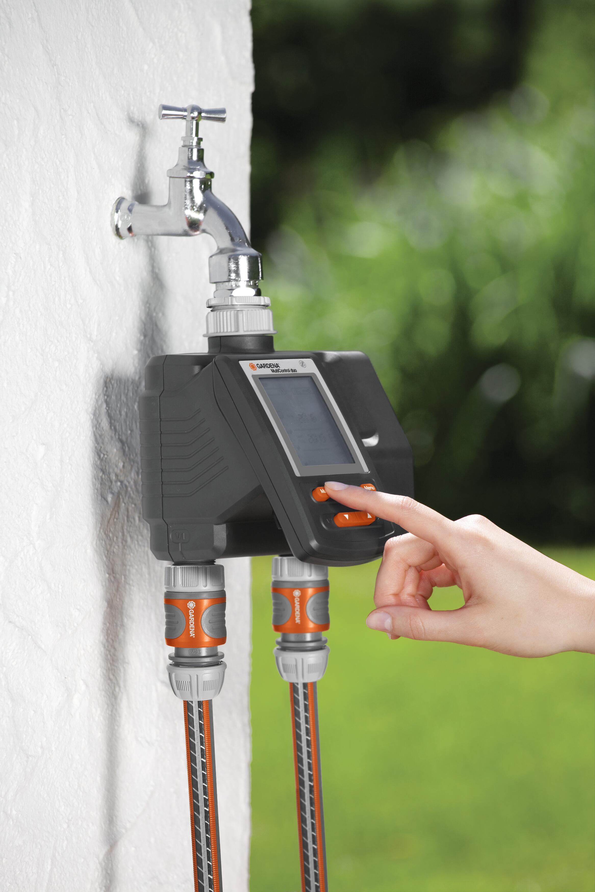 Una mano regola un timer per l'acqua collegato a un rubinetto con due tubi.