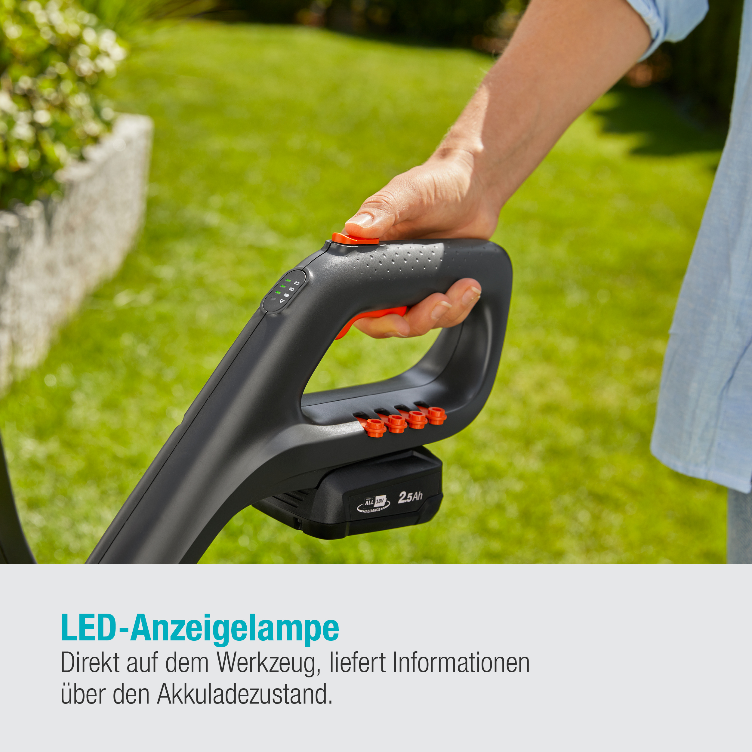 Nahaufnahme eines schwarz-grauen Trimmers mit rotem Knopf. Gras im Hintergrund sichtbar.