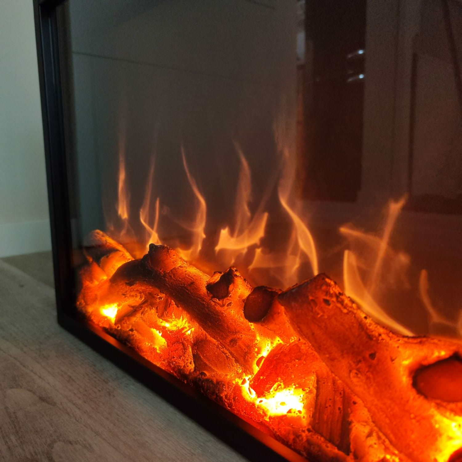 Nahaufnahme eines beleuchteten elektrischen Kamins mit orangefarbenen Flammen und Holzscheiten.