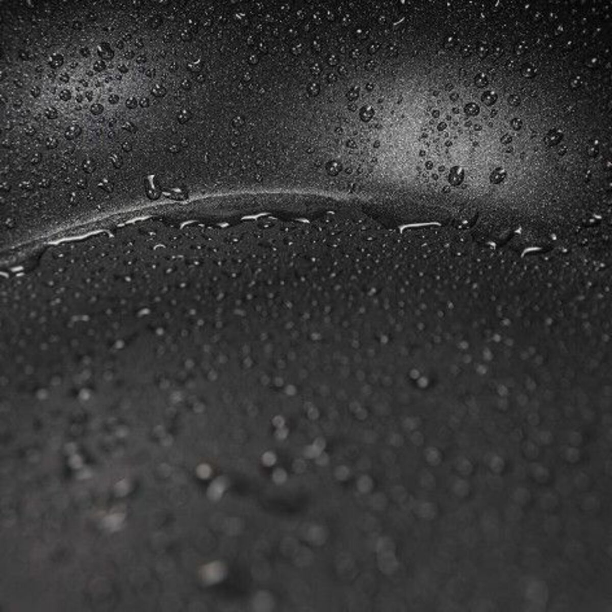Primer plano de una superficie de sartén oscura y húmeda con muchas gotas de agua.