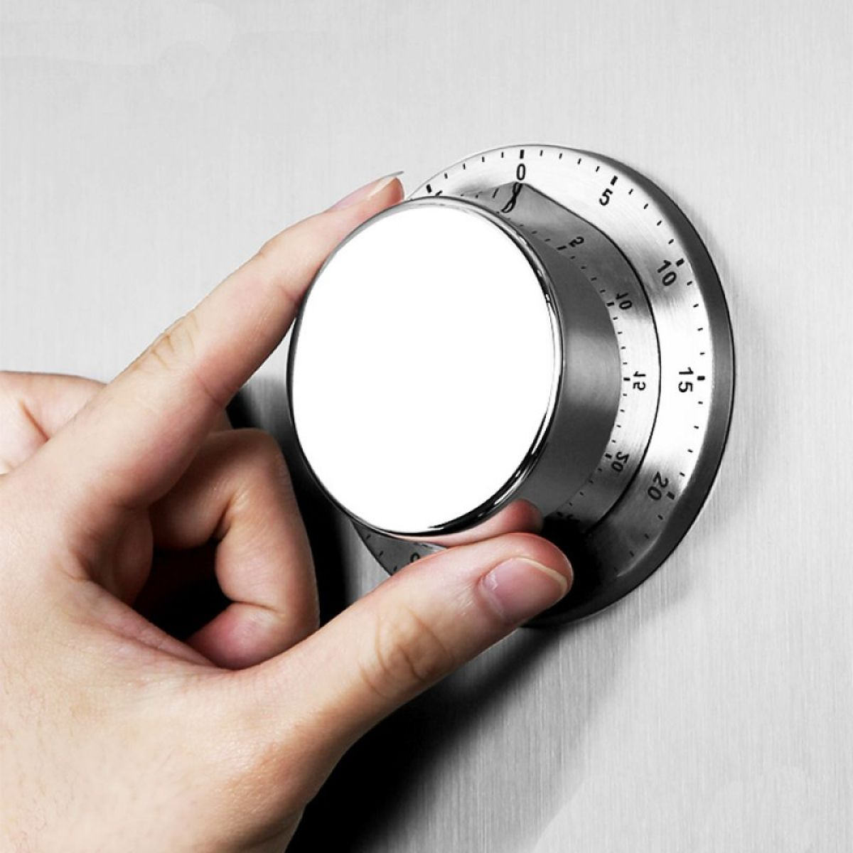 Eine Hand dreht einen silbernen Timer-Wählknopf. Das Zifferblatt ist rund mit einem weißen Zentrum und Zahlen.