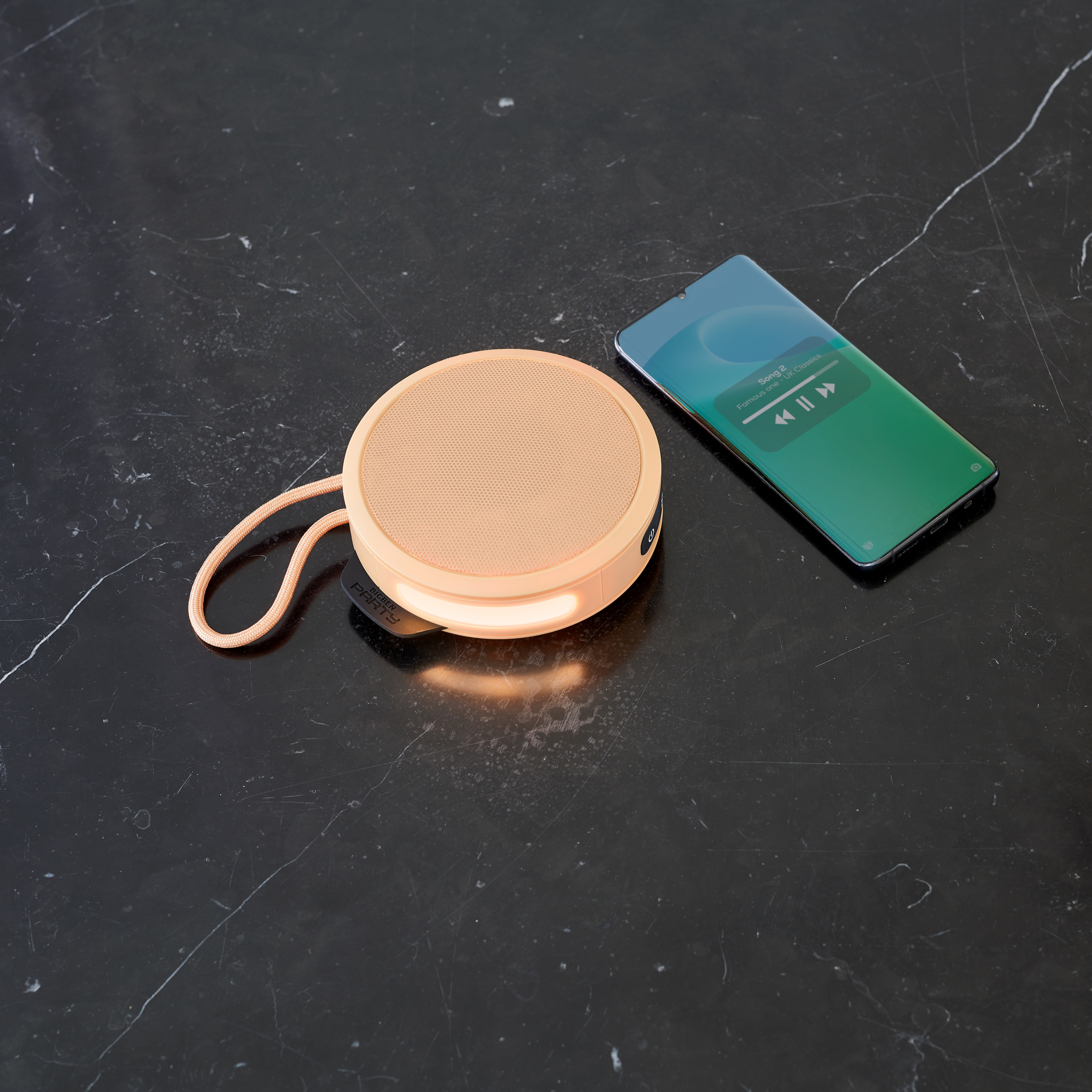 Brzoskwiniowy głośnik i telefon z muzyką, na ciemnej, teksturowanej powierzchni.