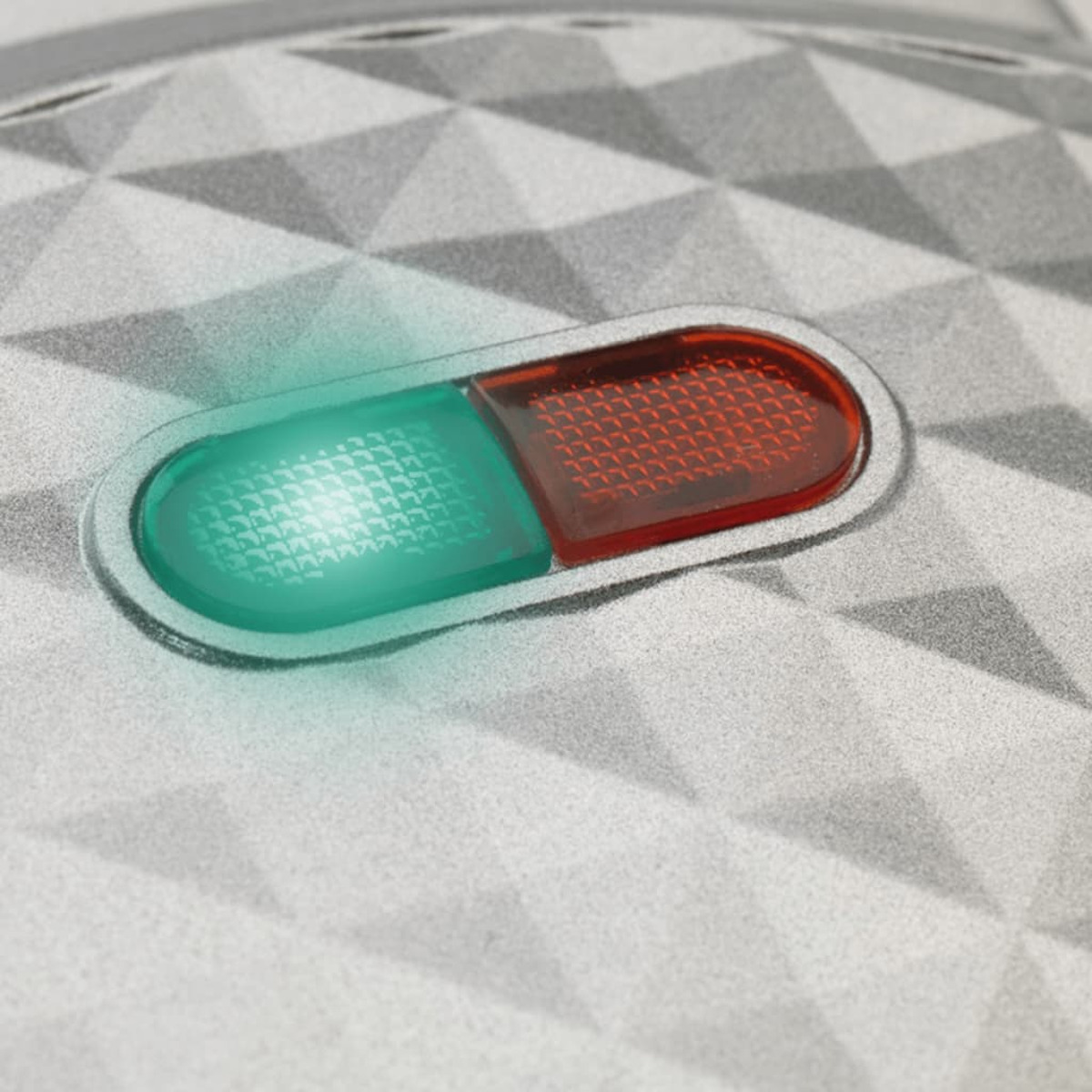 Una superficie plateada con un botón verde y rojo iluminado. Tiene forma ovalada.