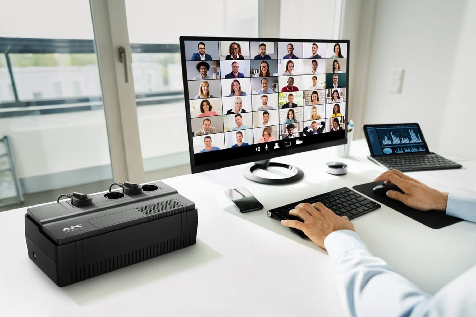 Osoba pisząca na klawiaturze z monitorem pokazującym wideokonferencję.